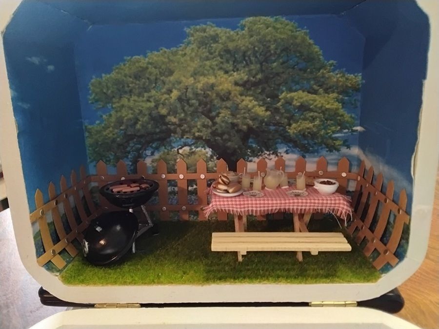 Miniature backyard diorama with tree, picnic table, bench, barbecue grill, and wooden fence