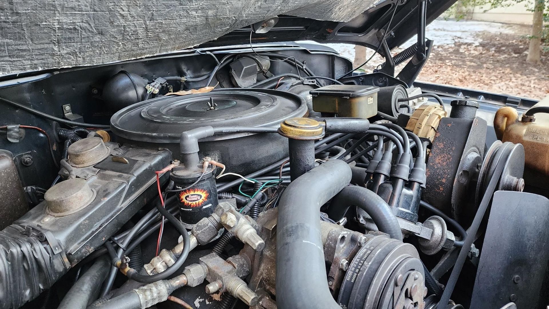 Engine bay of a black vehicle, hood open, showing air cleaner, hoses, belts, and various engine components.