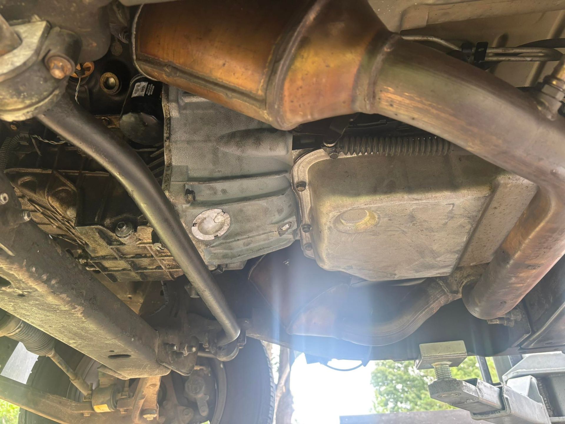 Undercarriage of a vehicle showing transmission, exhaust, and suspension components, with potential fluid leaks visible.