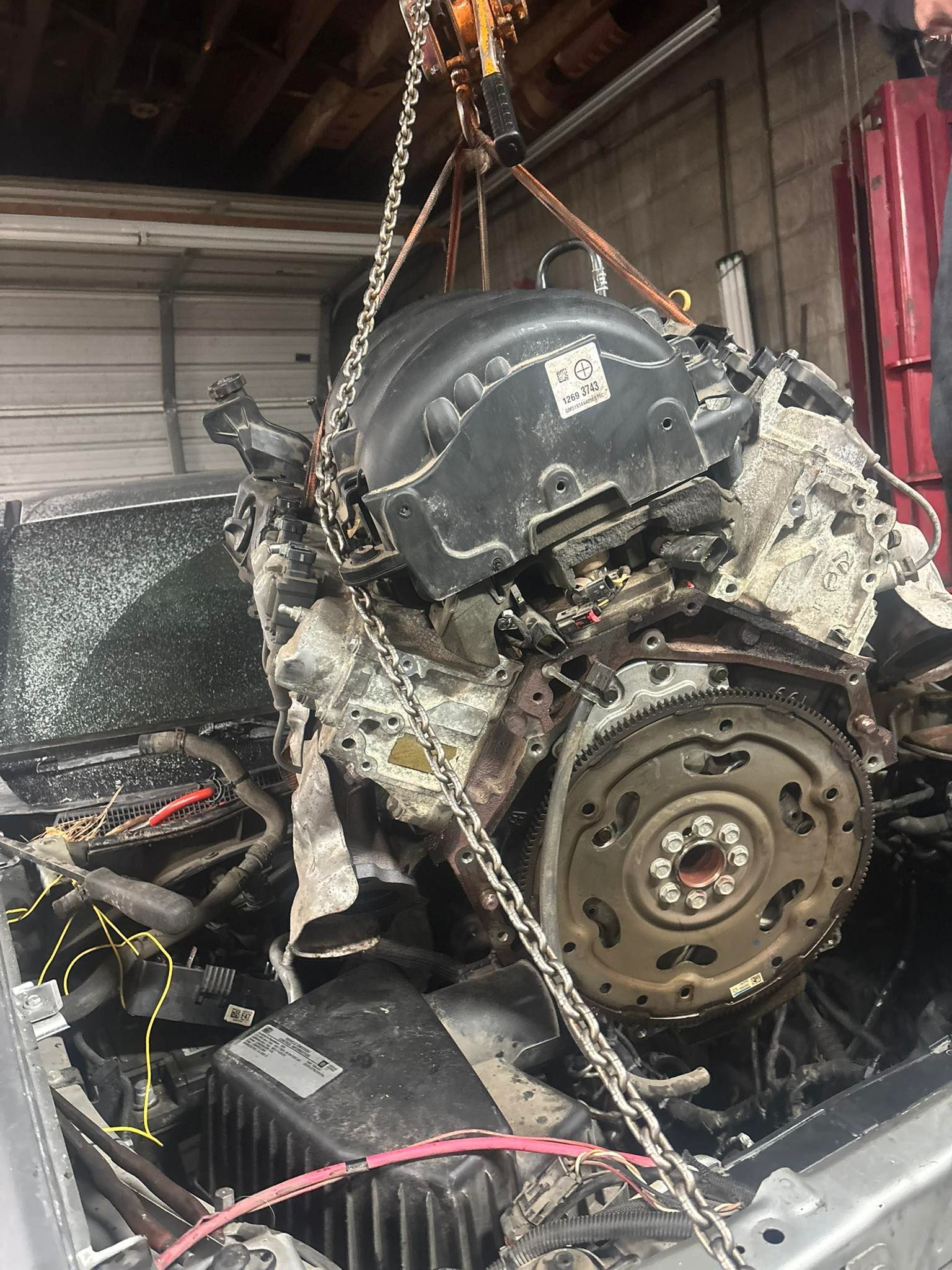 Engine being lifted from vehicle using a chain hoist inside a garage.
