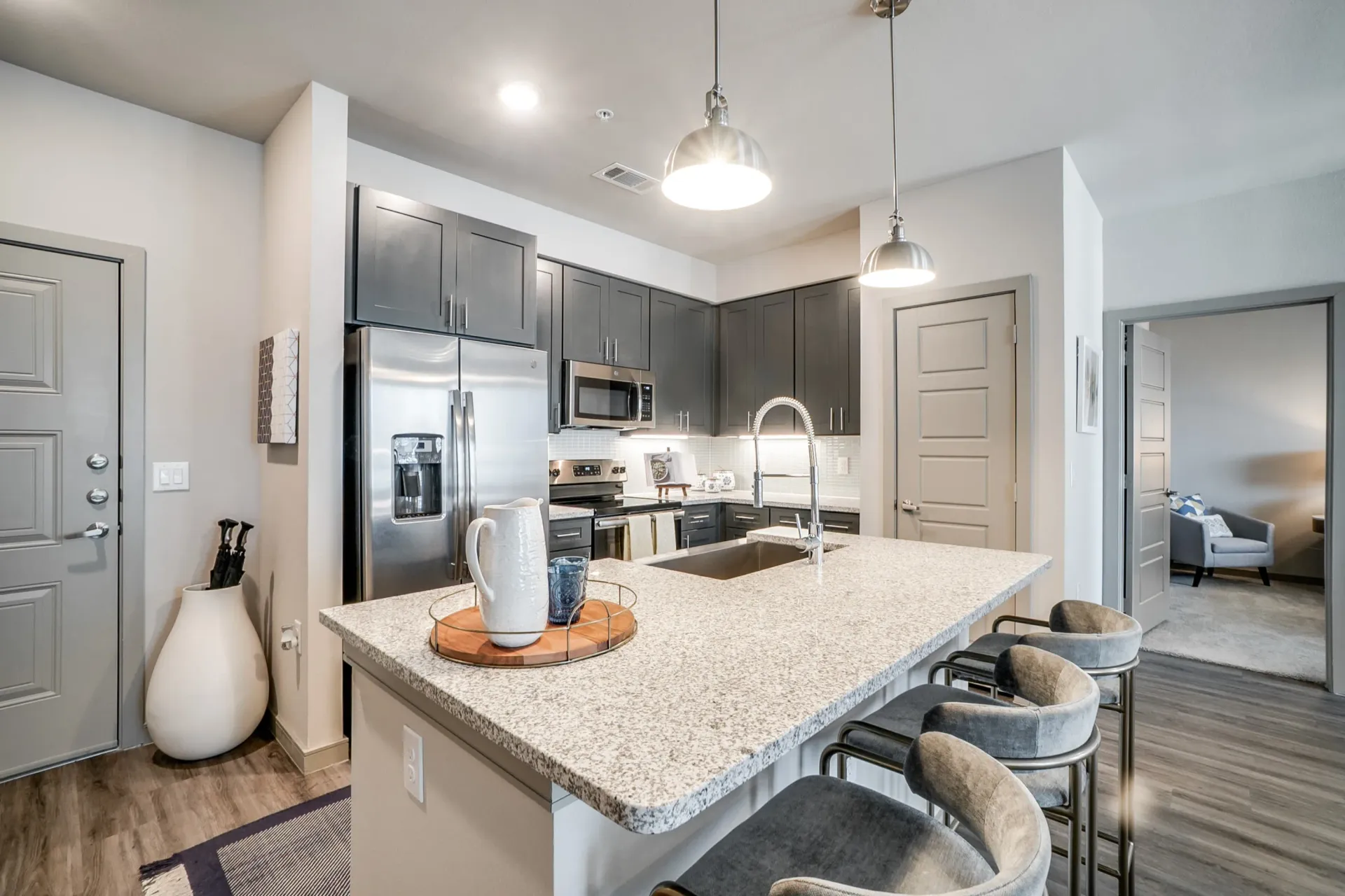 Modern kitchen with gray cabinets, granite island, and stainless steel appliances.