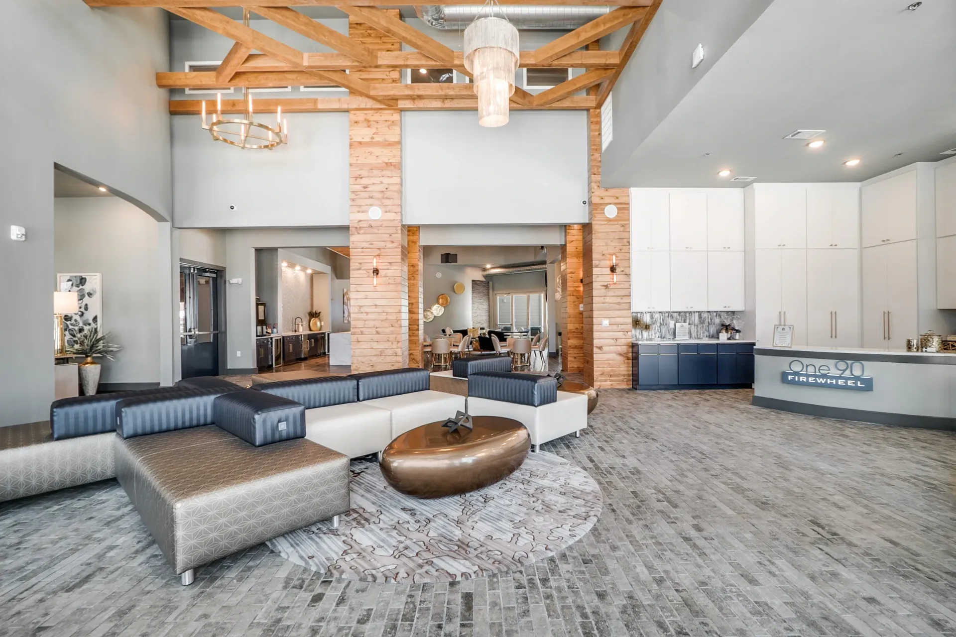 Modern apartment community lobby with curved sofas, wood beam ceiling, and a reception desk.