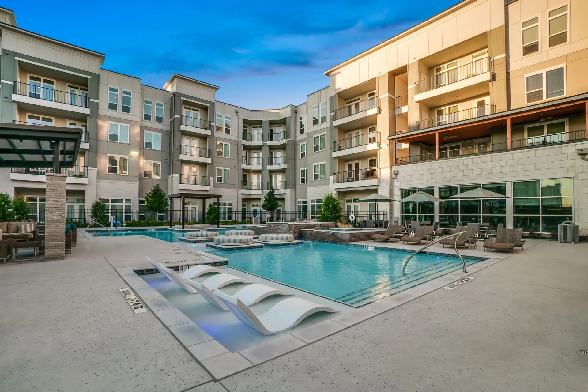 Outdoor pool area at a modern apartment community with lounge chairs and umbrellas.