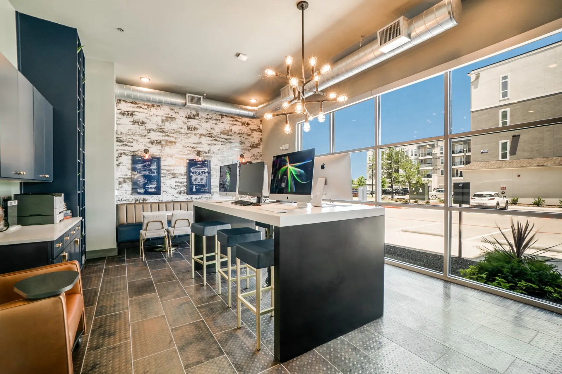 Modern community workspace with a long white desk, computers, and high stools by large windows.