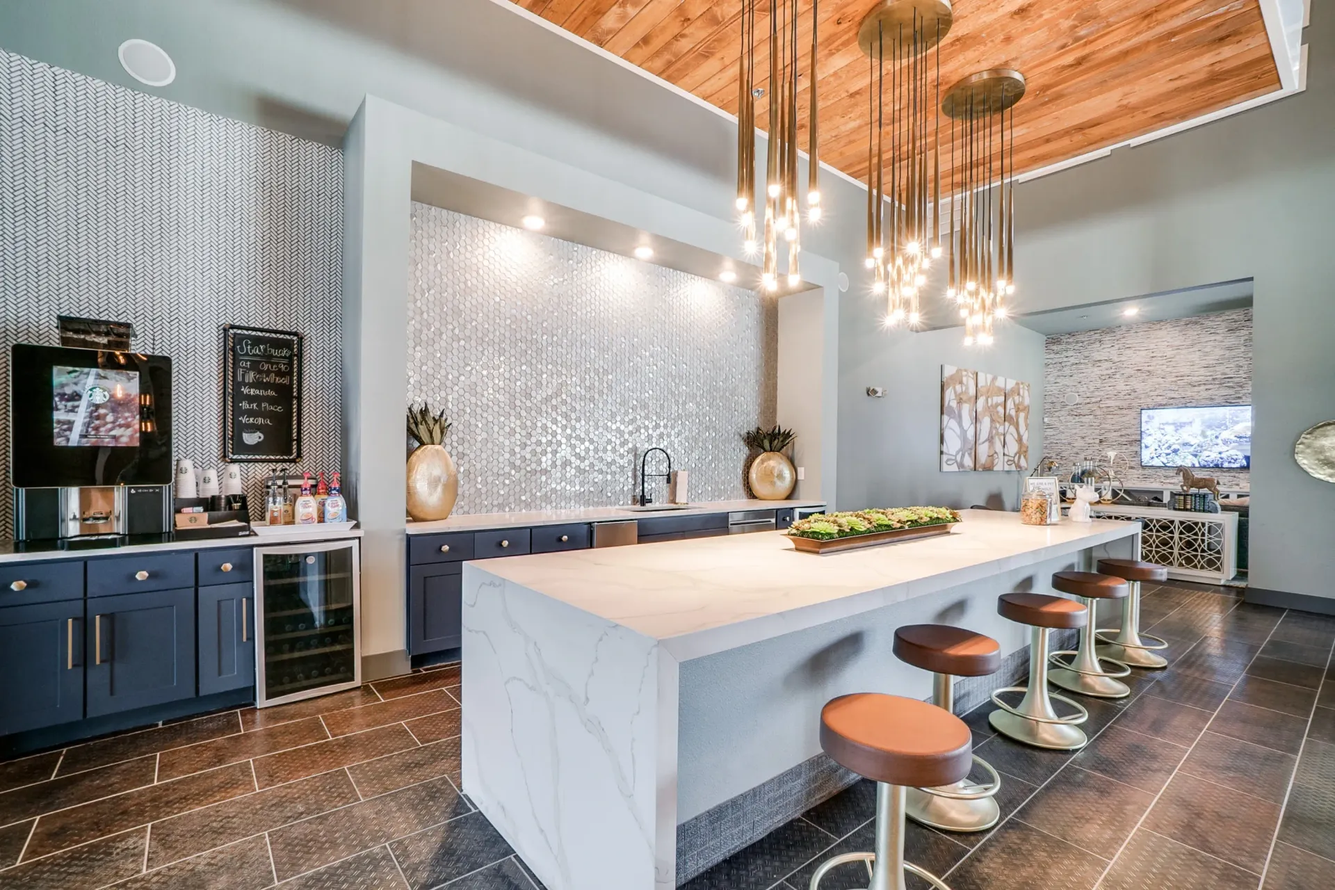 Modern community lounge with marble island, pendant lights, and a tiled backsplash.