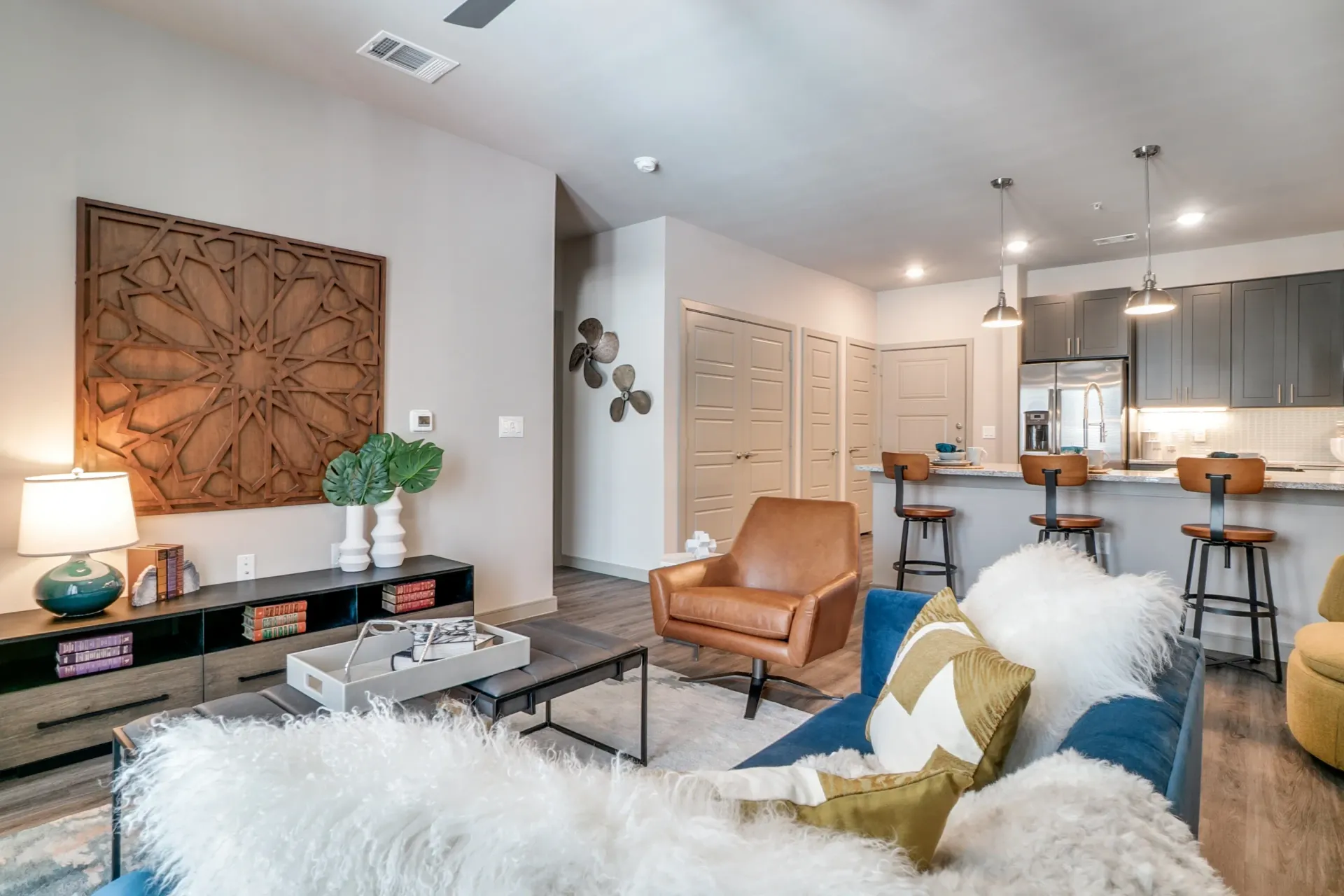 Open-concept living area with a blue sofa, brown leather chair, and kitchen island with bar stools.