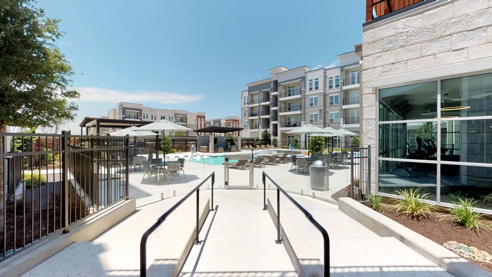 Outdoor pool area with lounge chairs and umbrellas among modern apartment buildings.