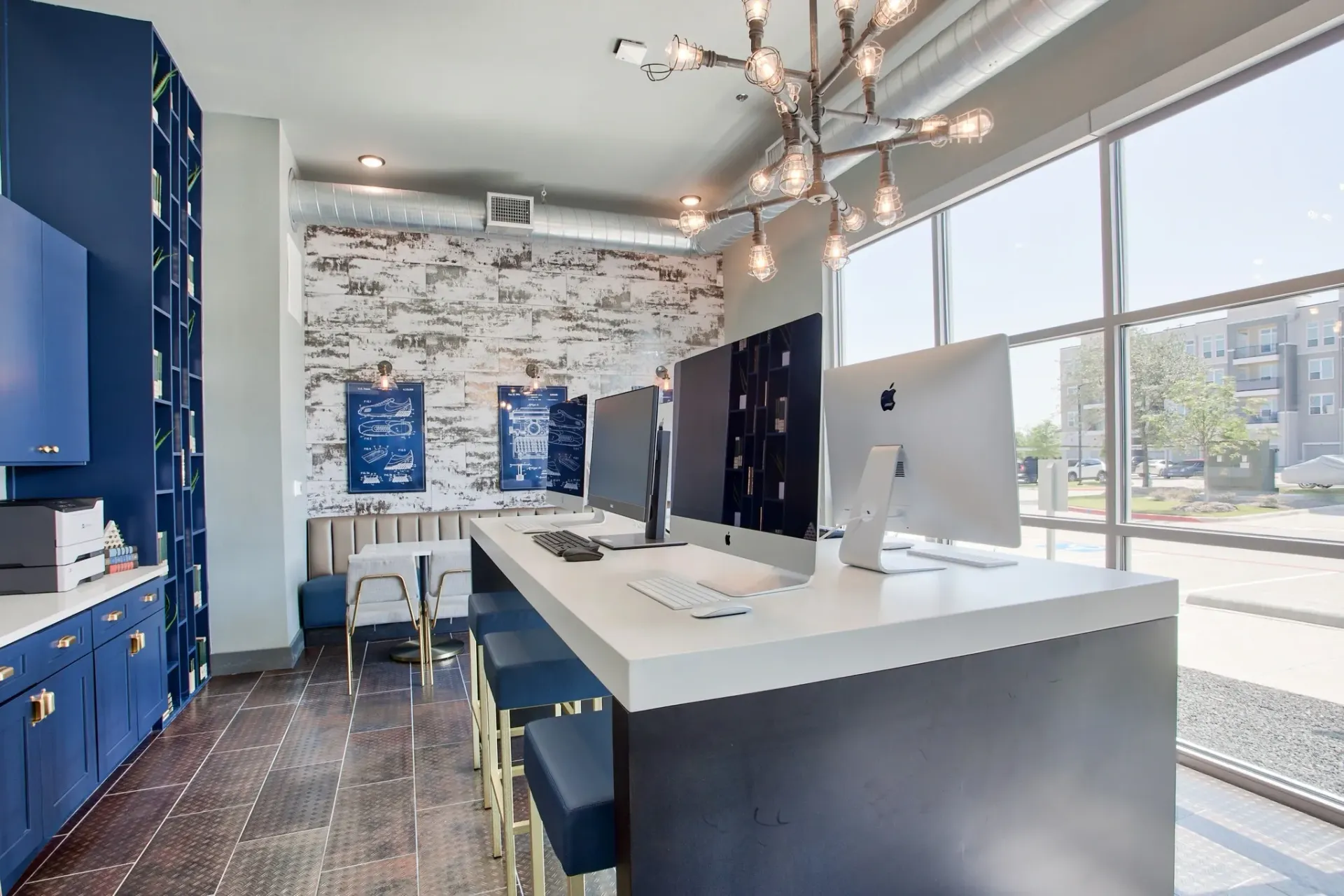 Modern community computer lounge with iMacs at a long counter, blue cabinets, and large windows.