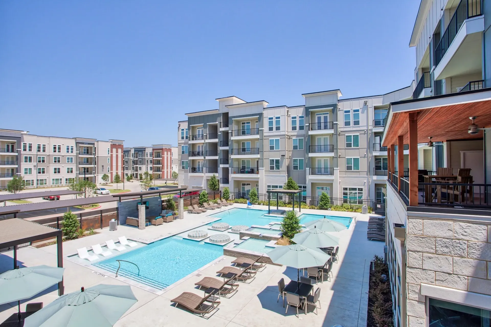 Outdoor pool area of a modern apartment complex with lounge chairs and umbrellas.