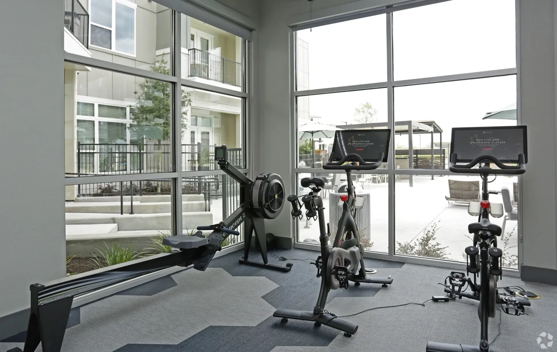 Indoor community fitness center with stationary bikes and a rowing machine by large windows.