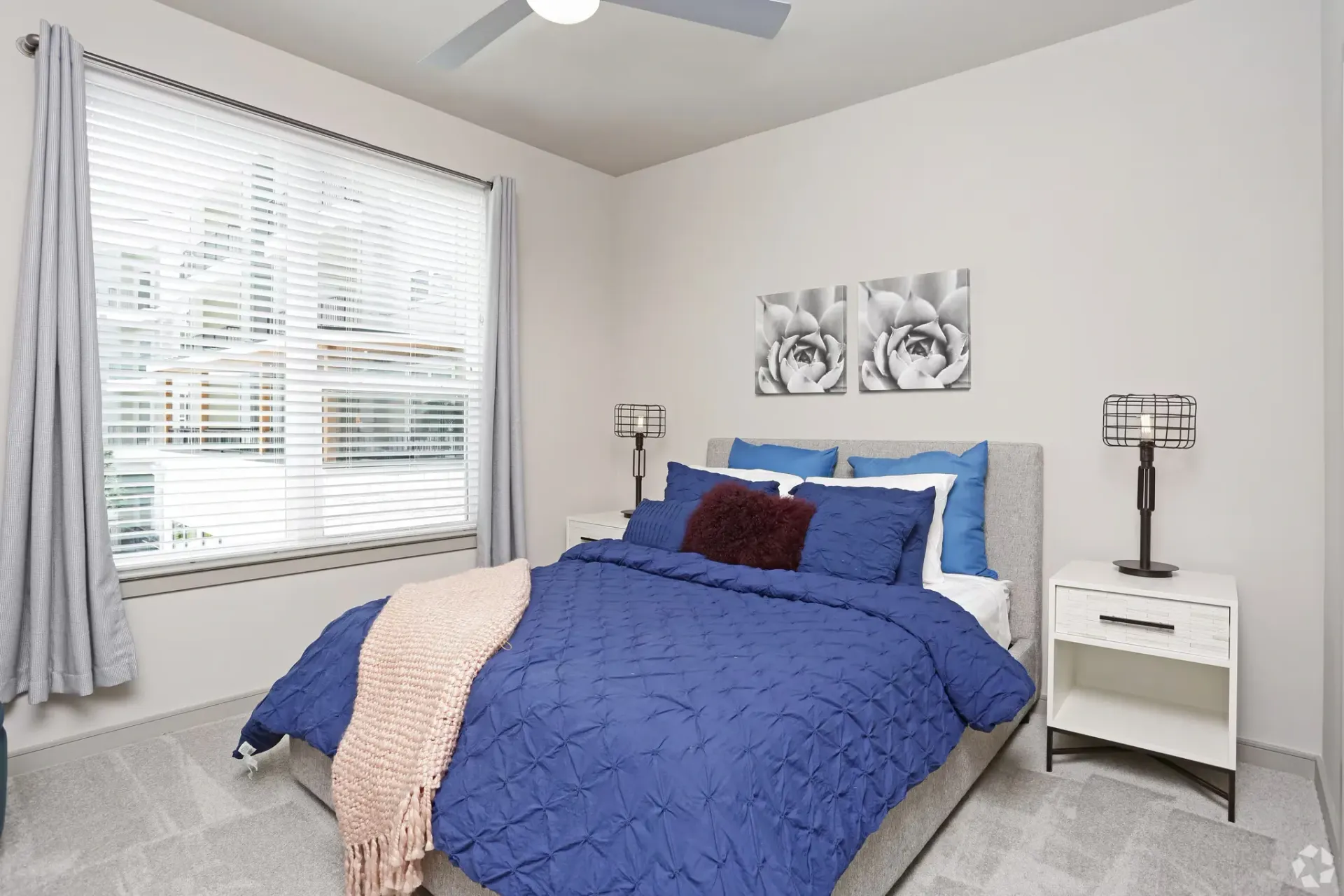 Bedroom in a modern apartment with a gray upholstered bed, blue bedding, and white nightstands.