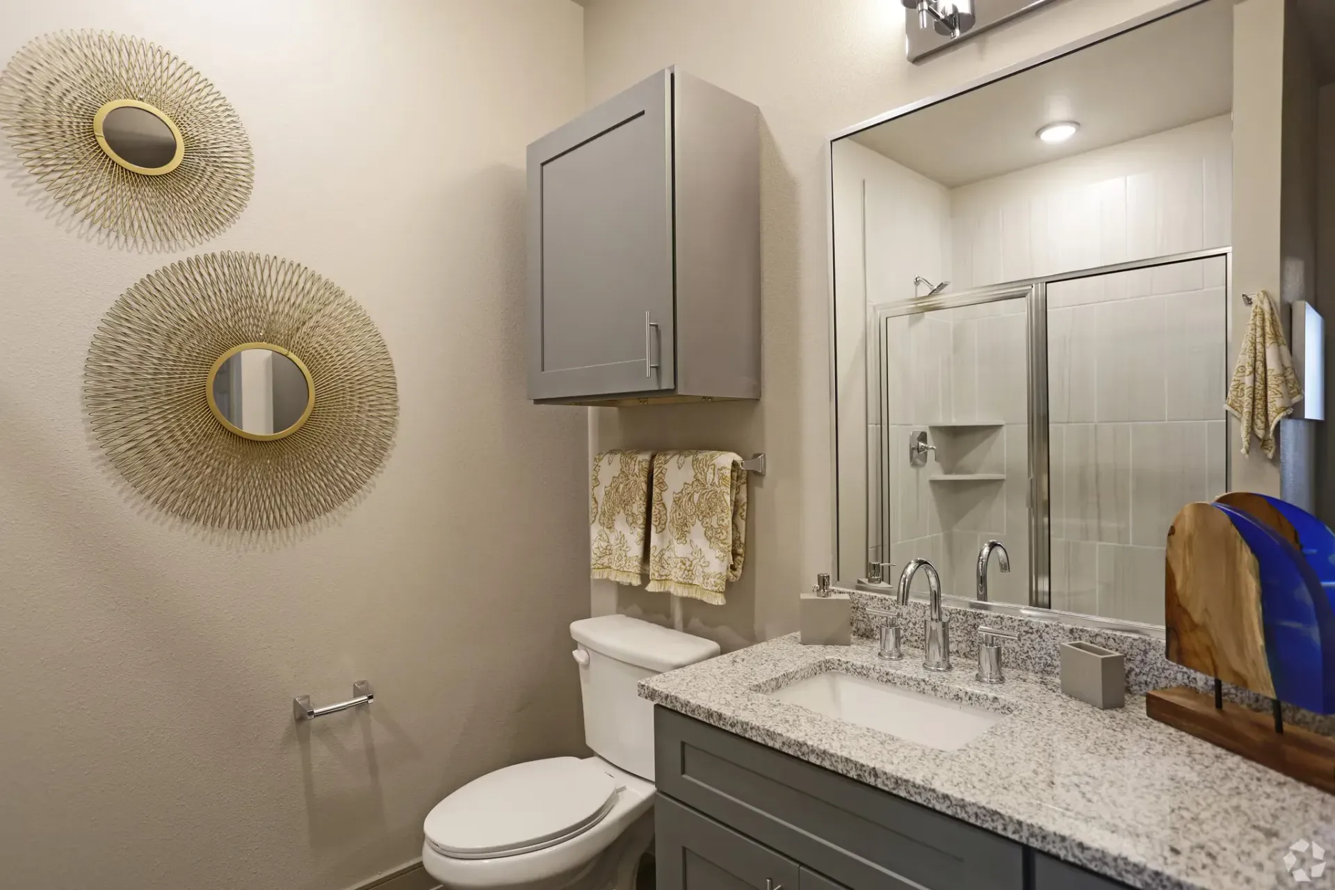 Bathroom featuring a granite countertop, gray vanity, large mirror, toilet, and glass shower.