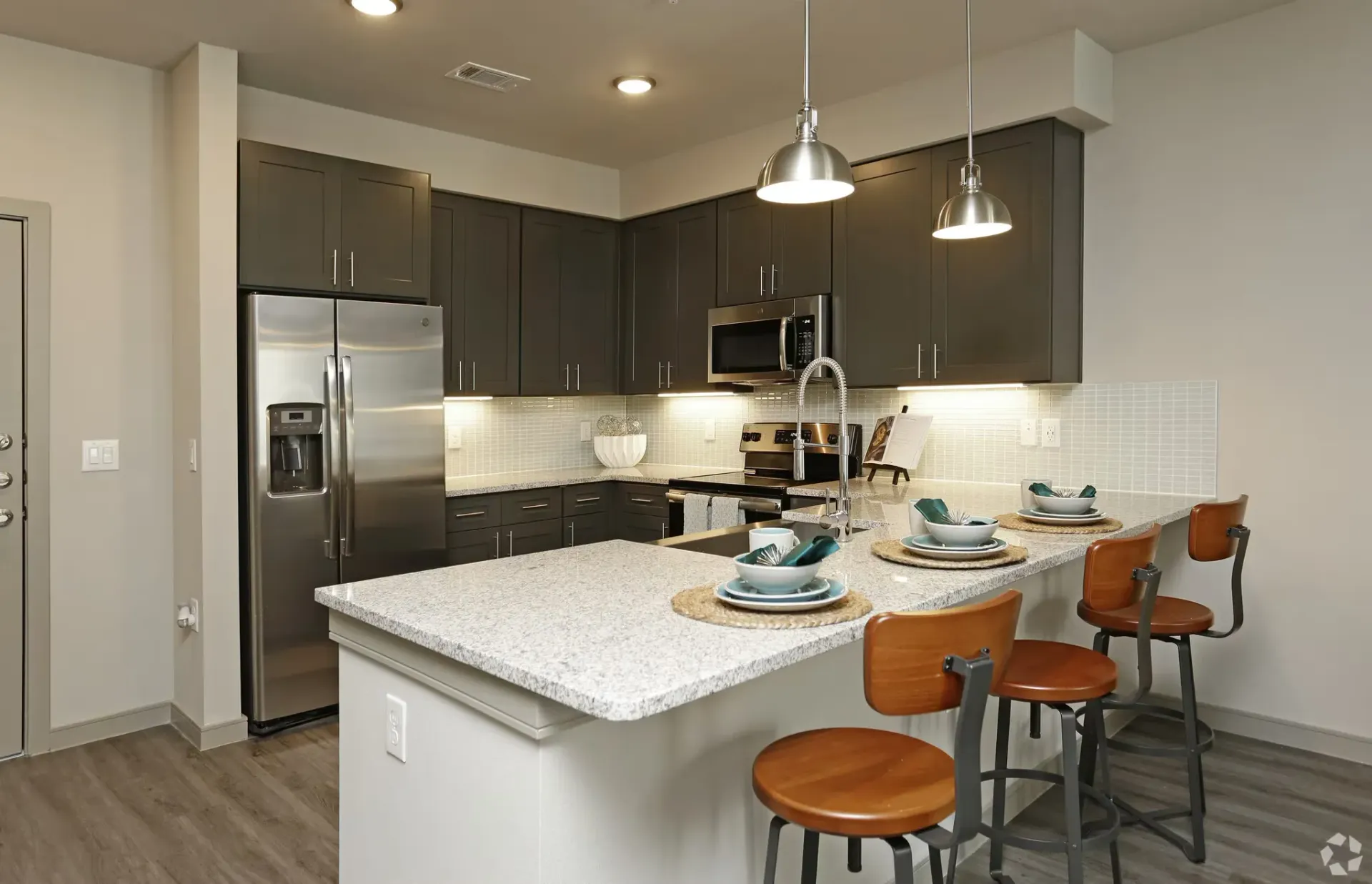 Open-concept kitchen with dark cabinets, island seating, and stainless-steel appliances.