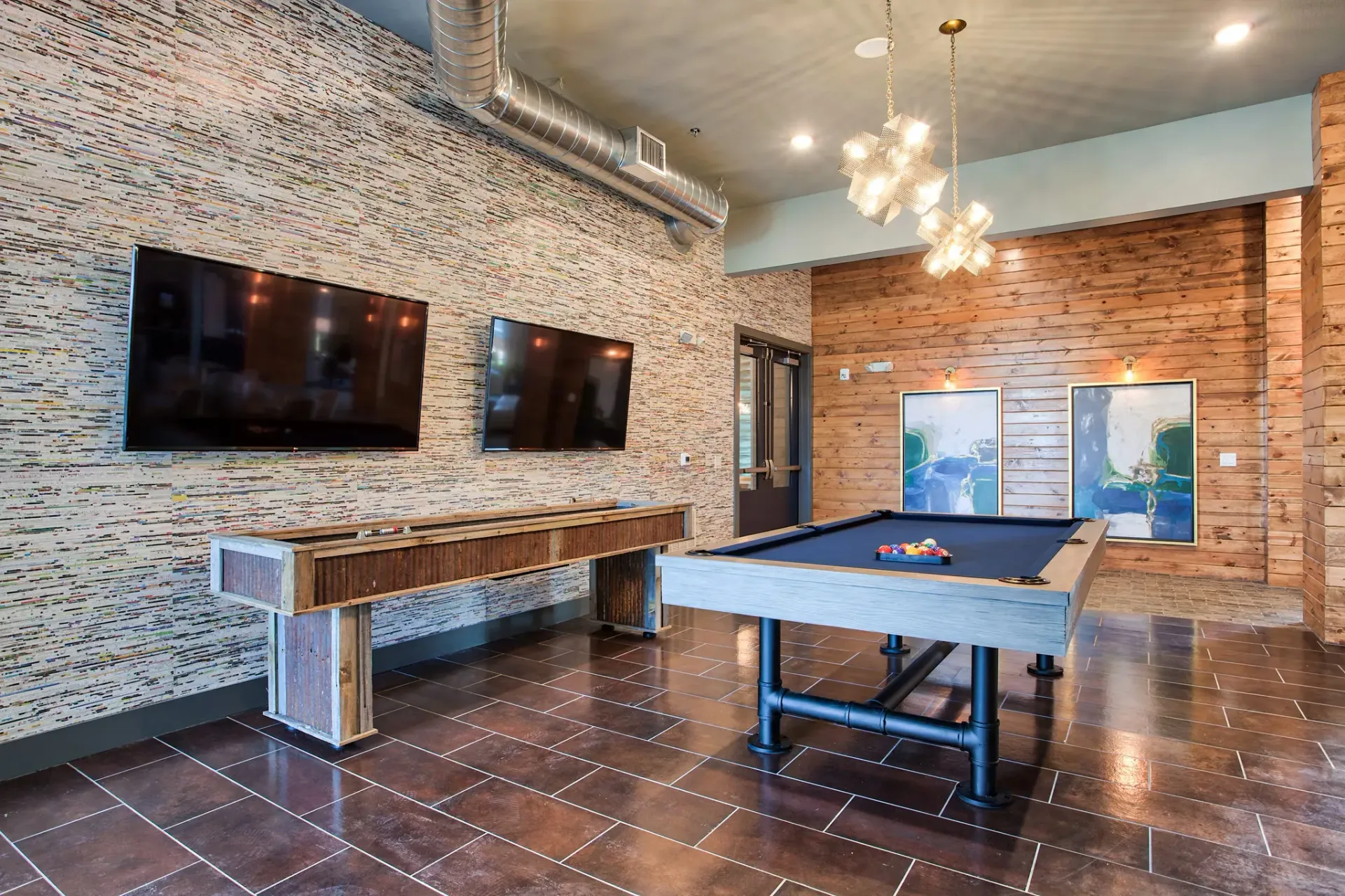 Indoor community game room with a pool table, two TVs, and wood panel walls.