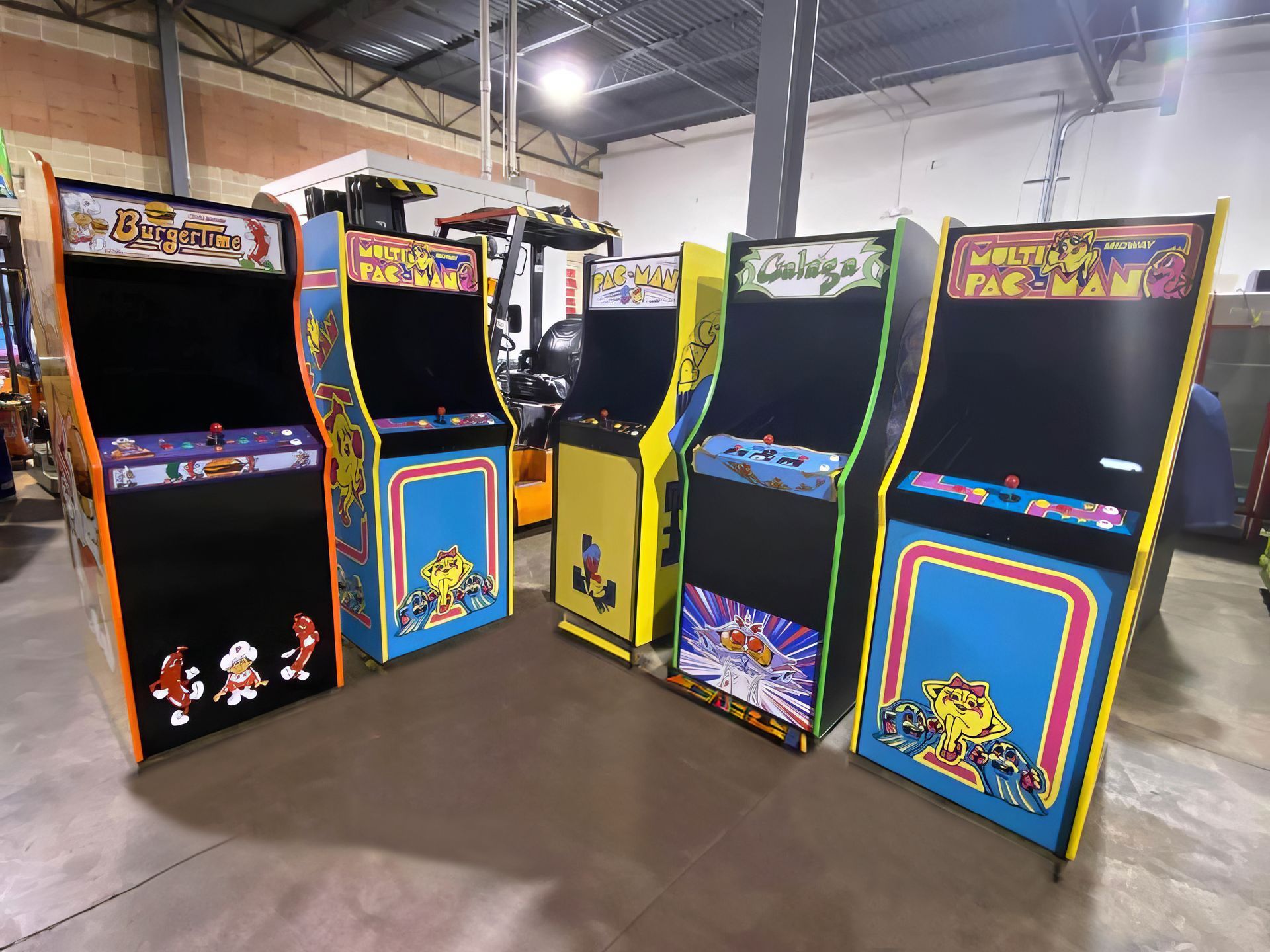 A row of arcade machines are lined up in a warehouse.