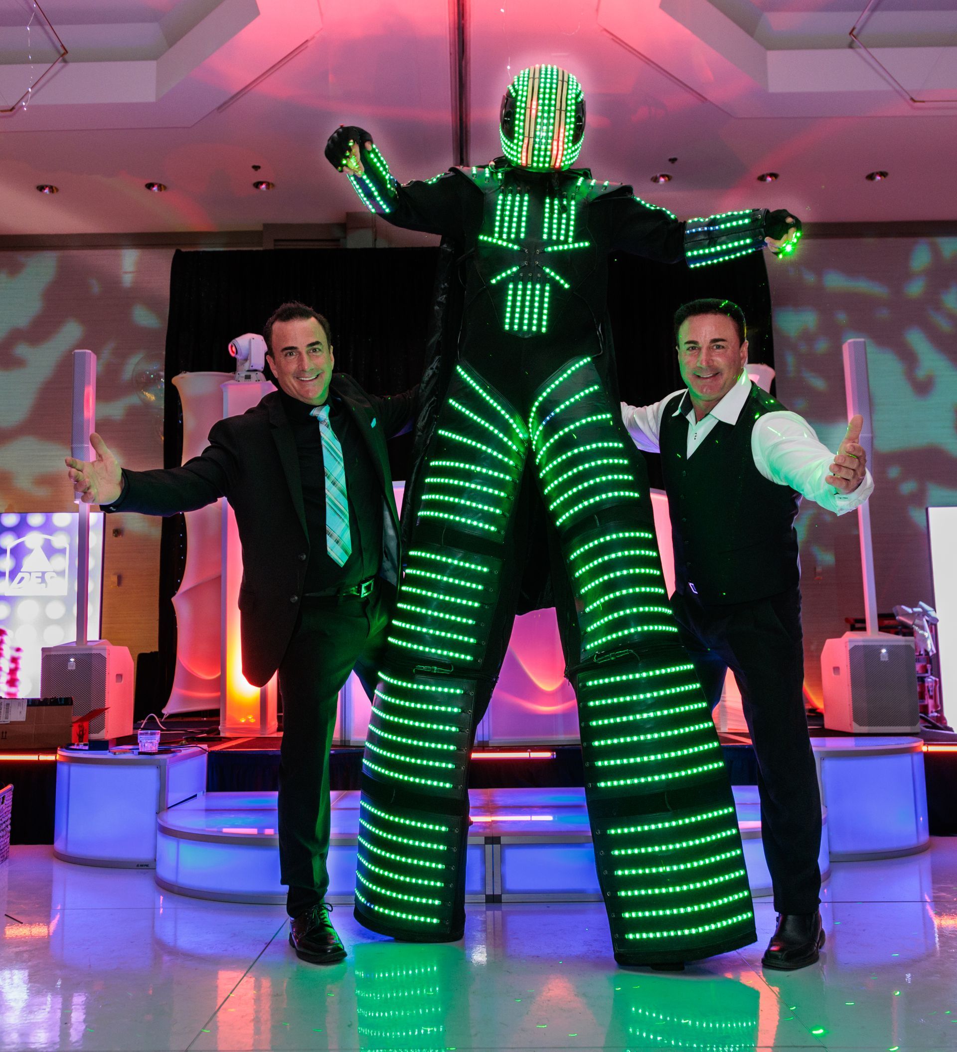 Two men are standing next to a robot dressed in green lights.