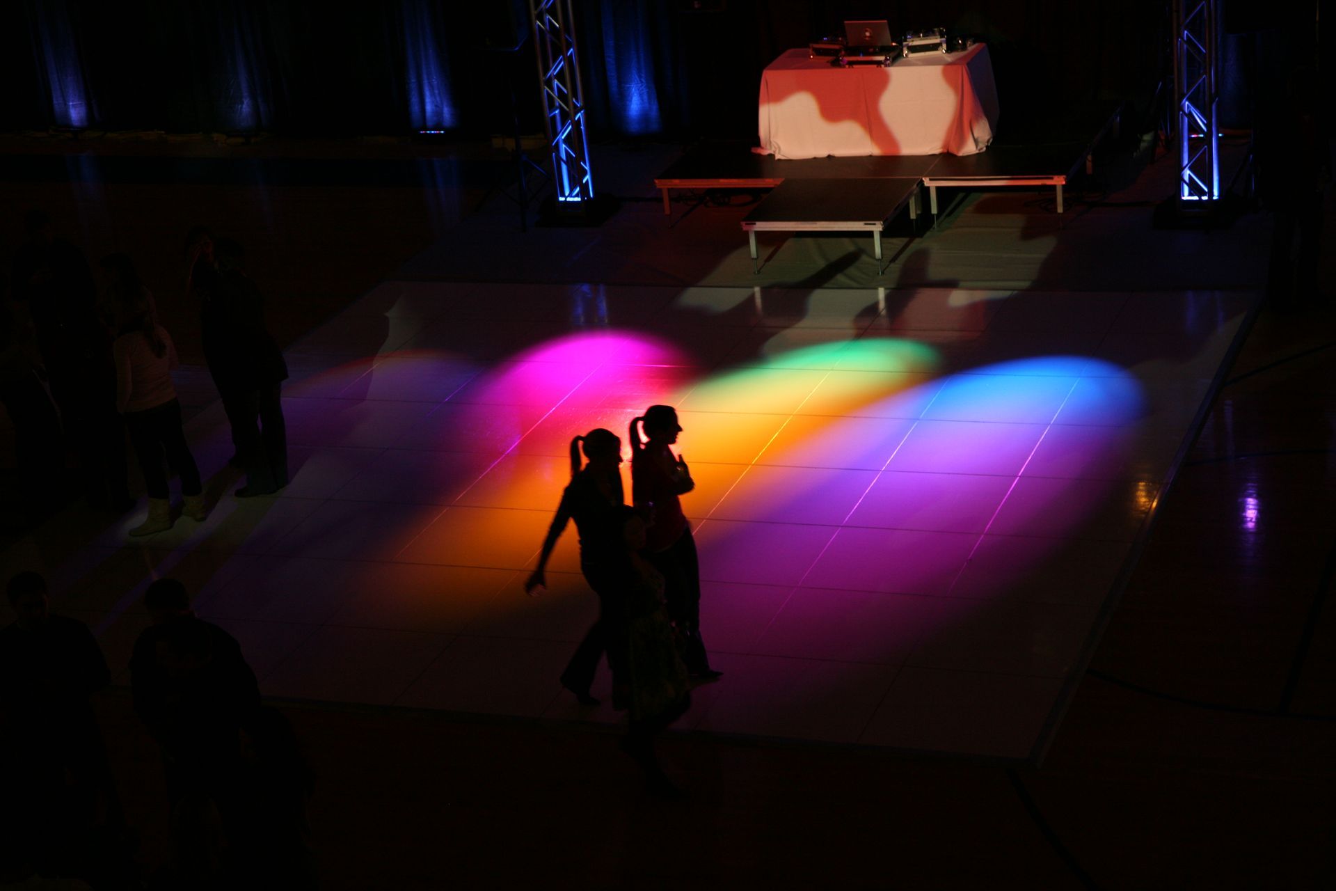 A couple is dancing on a dance floor with colorful lights projected on it.