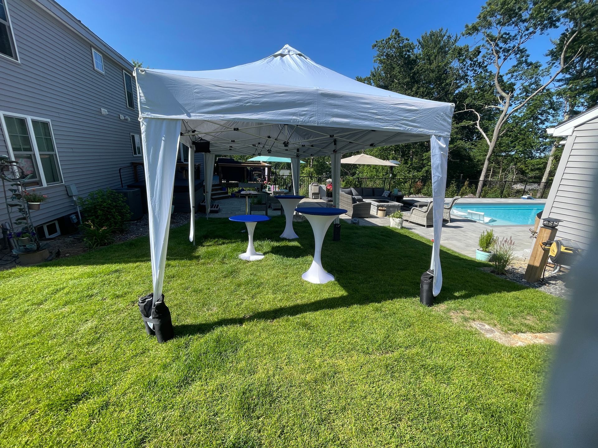 A white tent is sitting on top of a lush green lawn next to a pool.