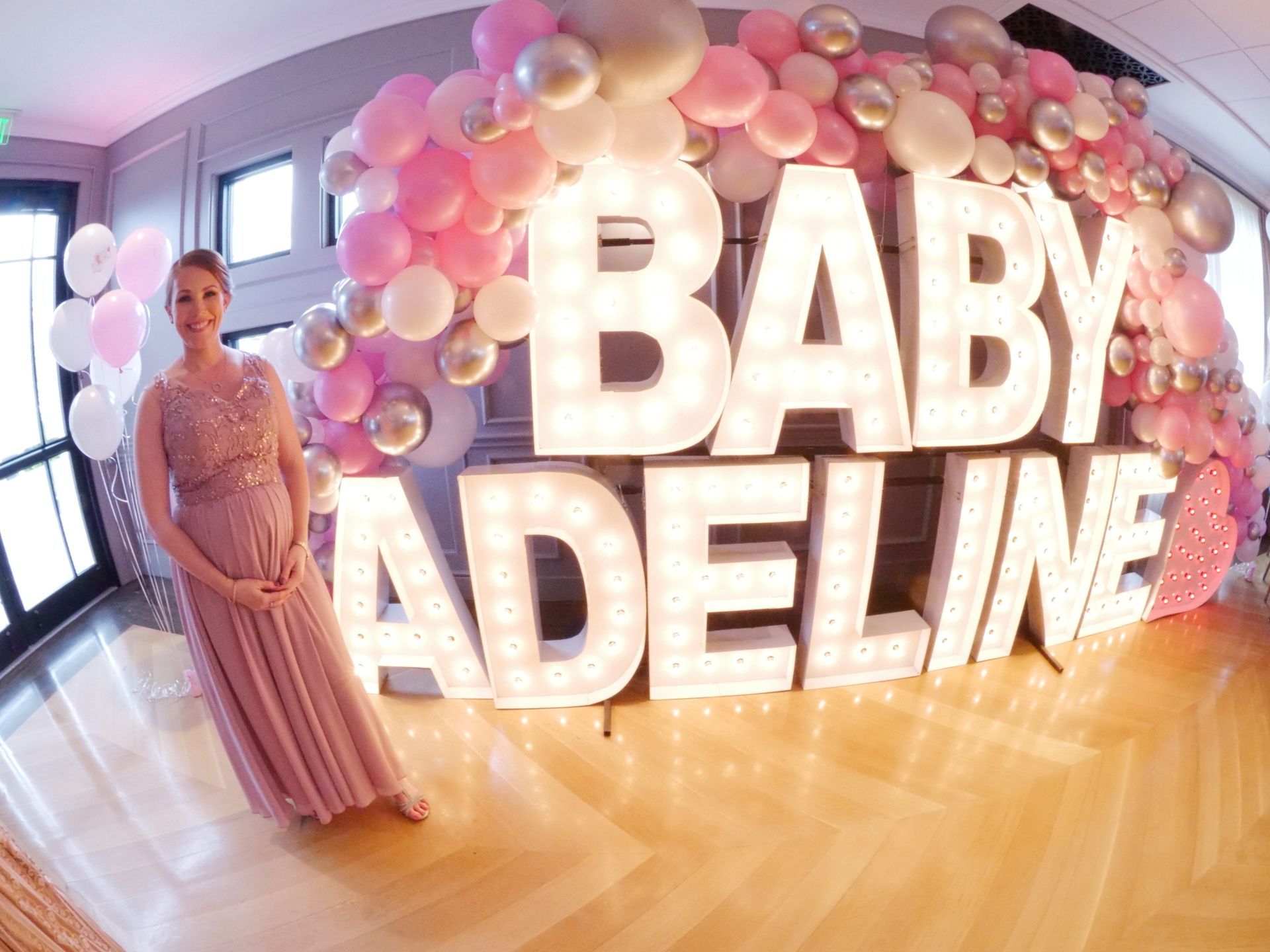 A pregnant woman is standing in front of a baby shower decoration.