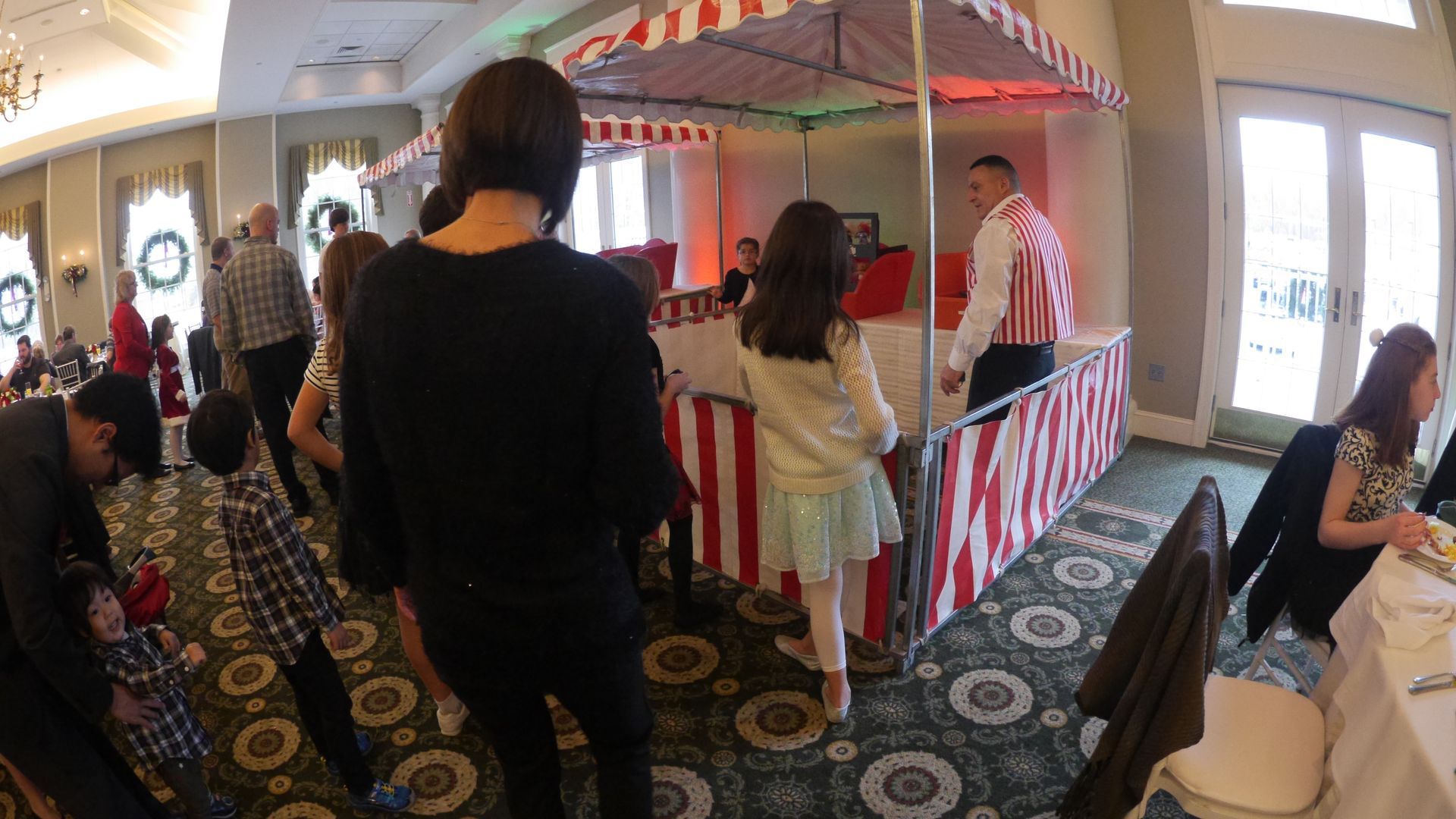A group of people are standing around a carnival booth event rental in a room.