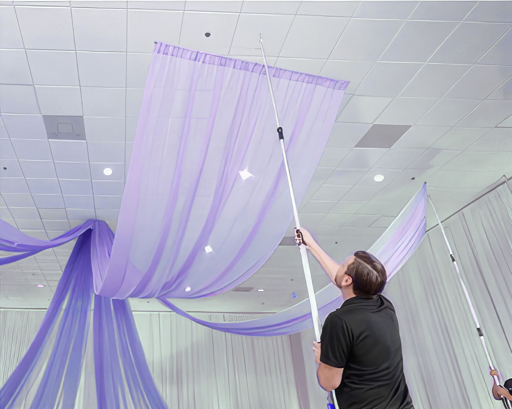 A man is hanging purple curtains from the ceiling of a room.