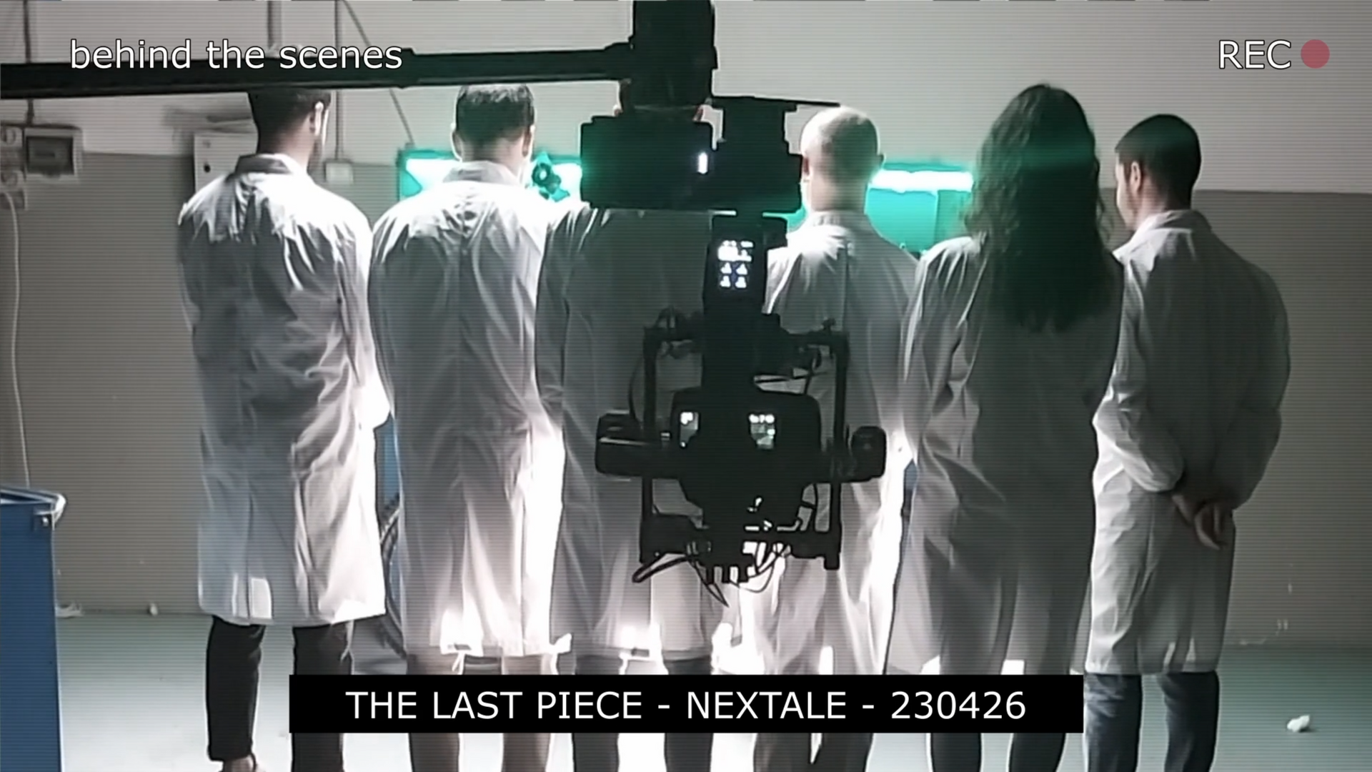 Behind the scenes of a film set: Five people in lab coats watch a camera rig. Blue and green lighting.