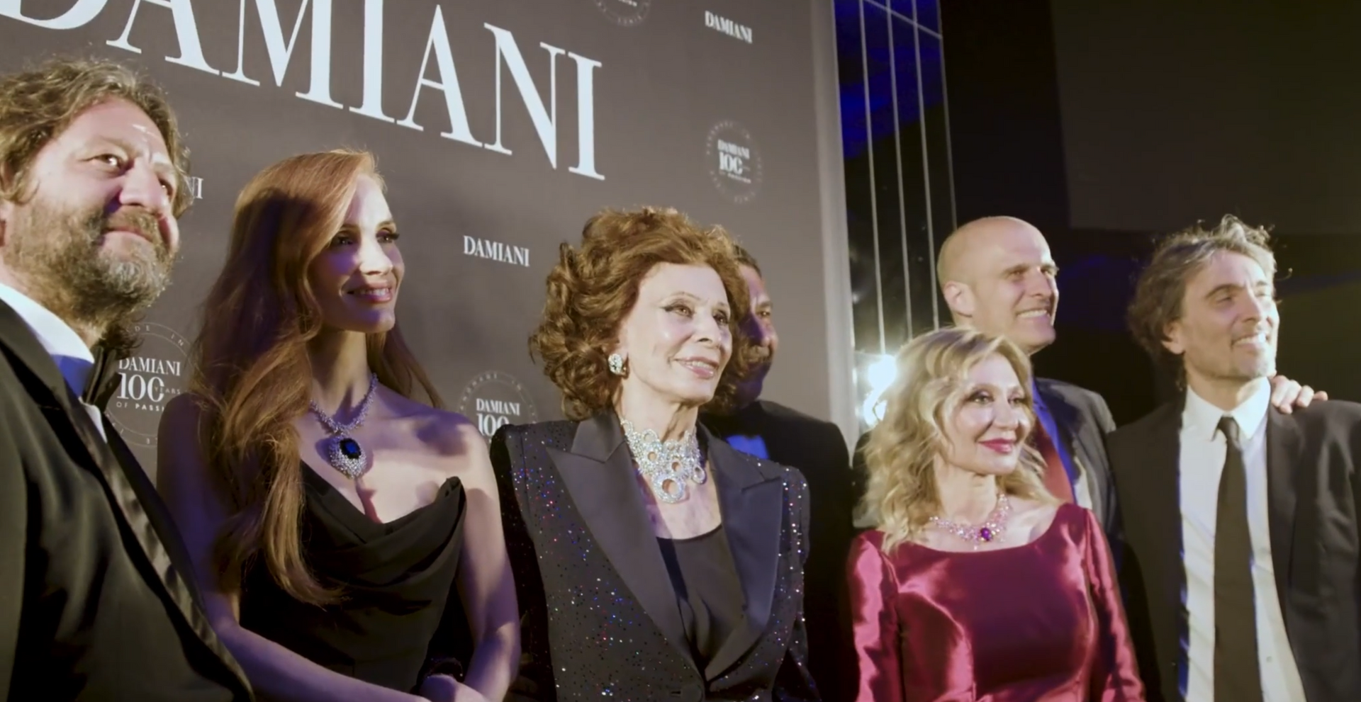 Group of people pose at a Damiani event; woman in a black jacket smiles.