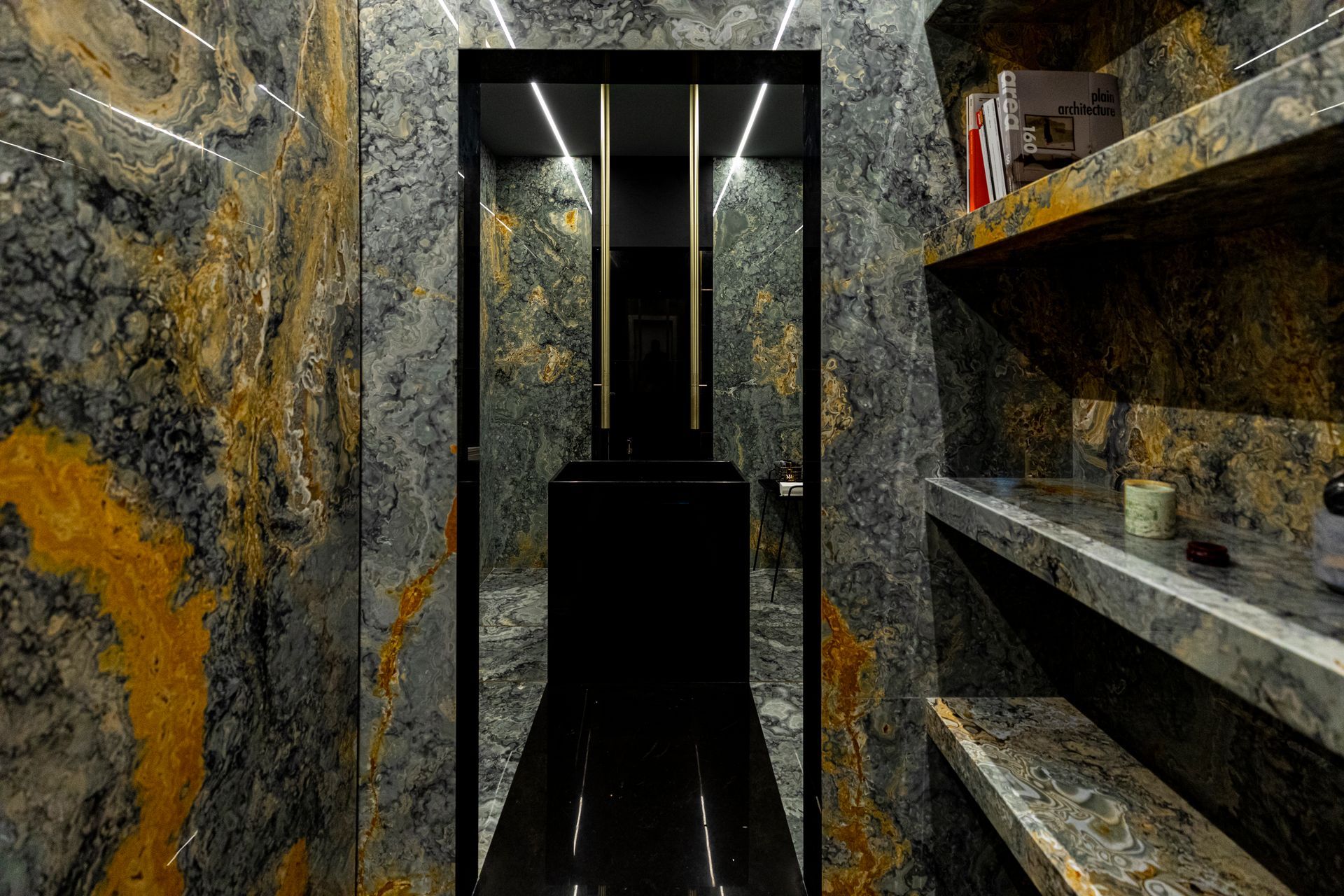 Dark, luxurious room with marble walls, black elevator, and floating shelves with objects.