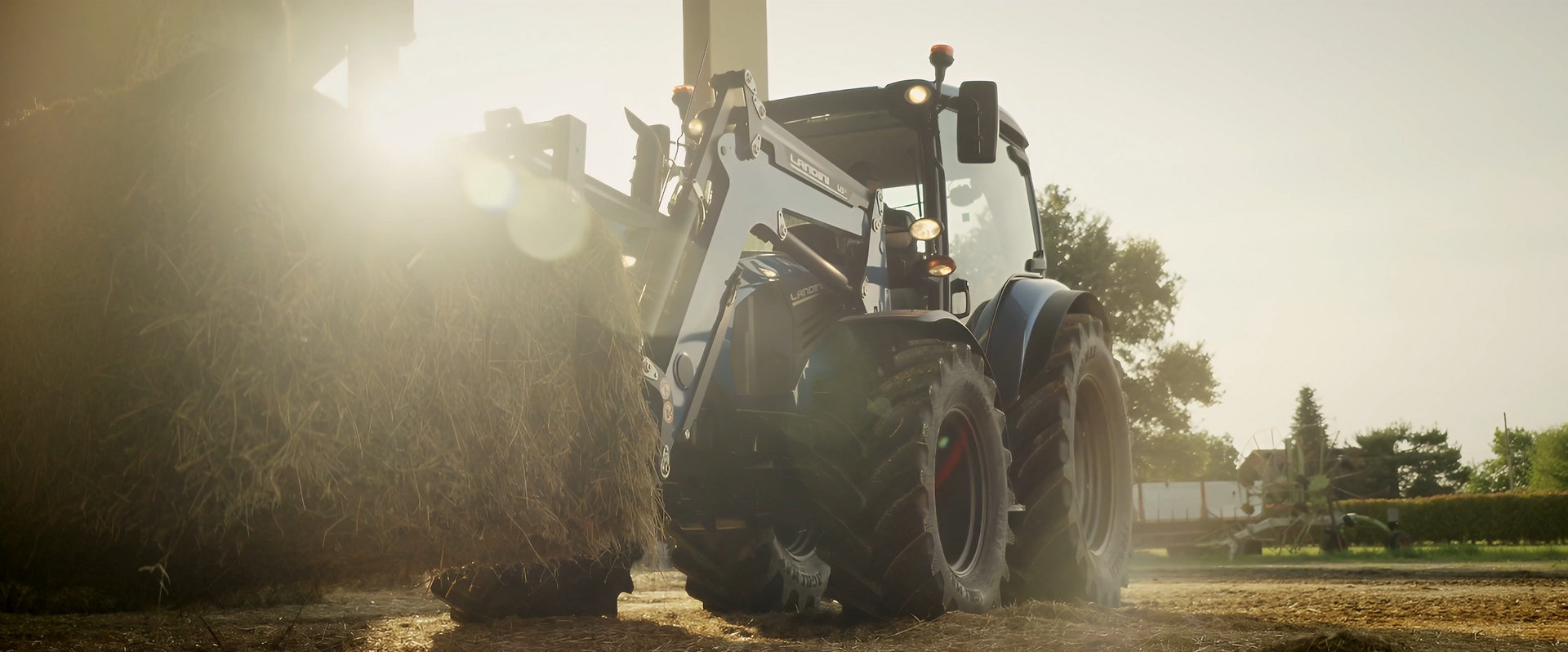 Tractor with a front loader, moving on a farm field with the sun shining in the background.