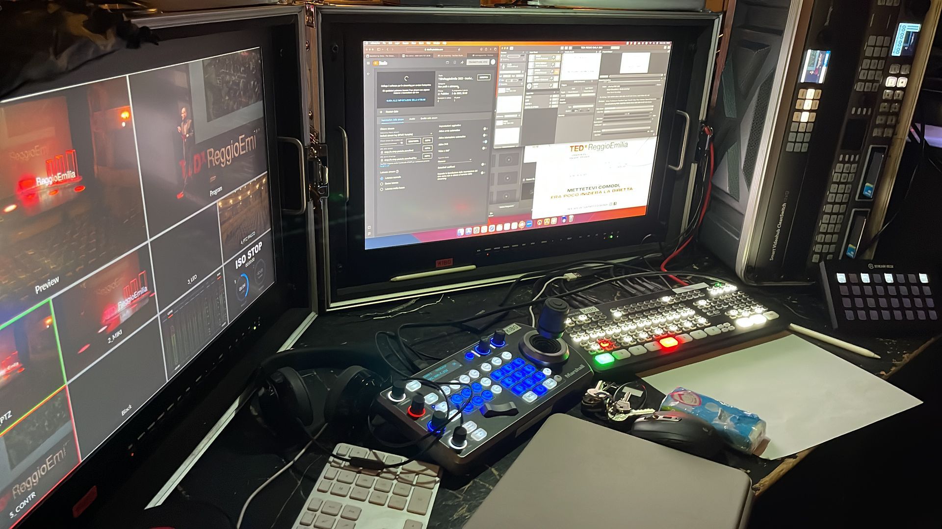 Video production control room with monitors displaying camera feeds, computer interface, and control panel.