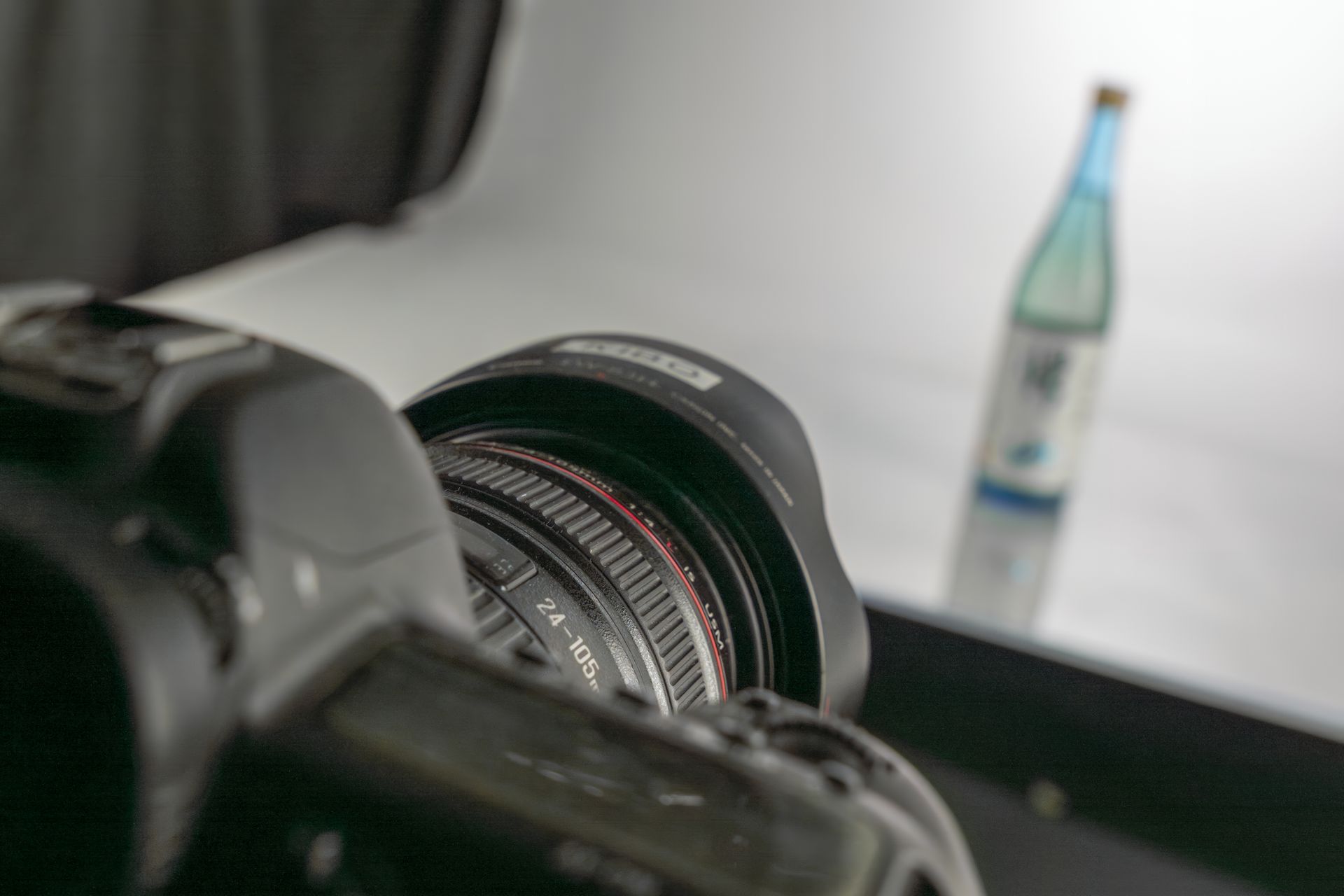 Camera lens focusing on a water bottle, placed on a reflective surface.