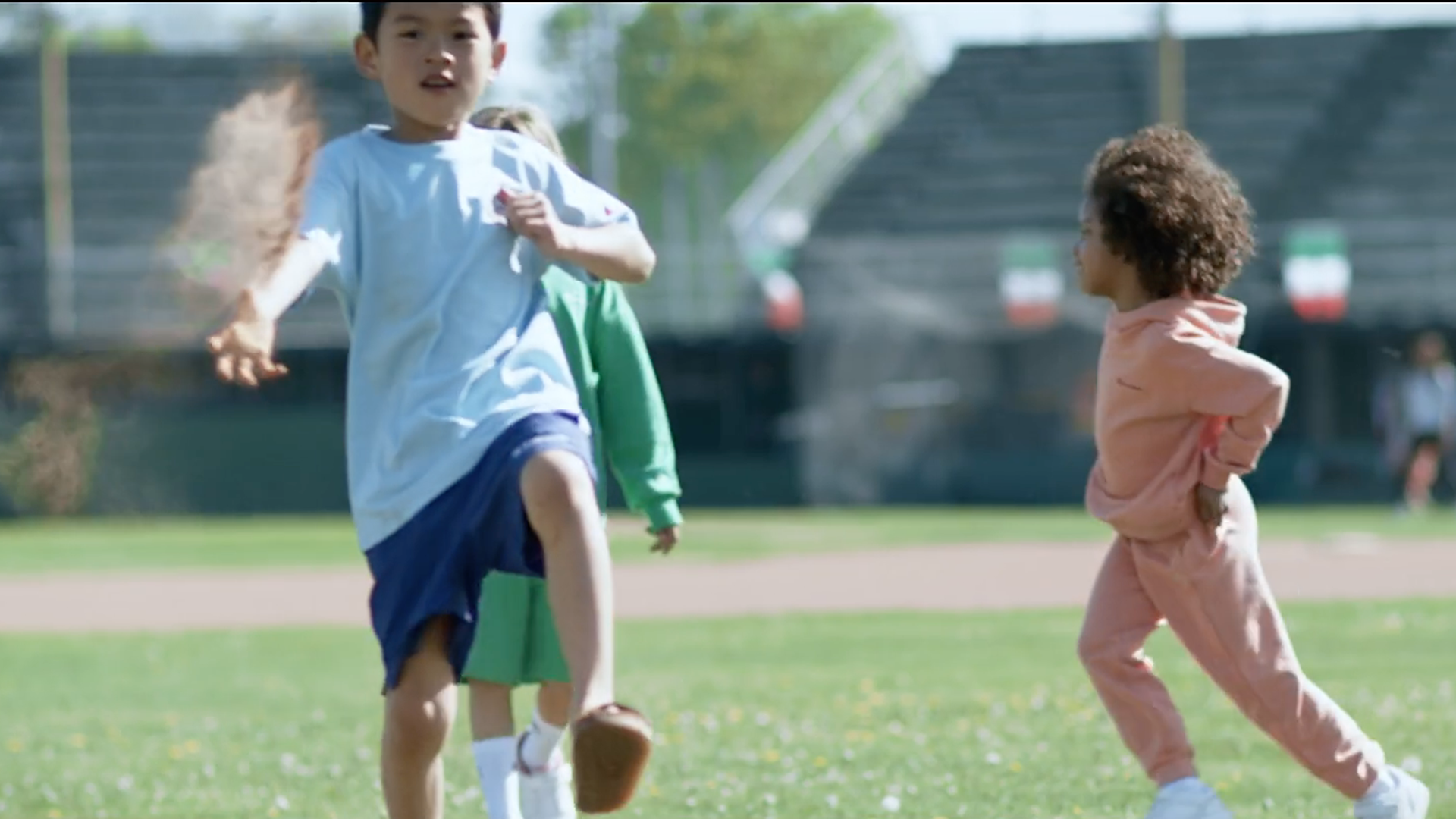 Children playing tag on a grassy field; one boy runs, another watches, powder cloud in the air.