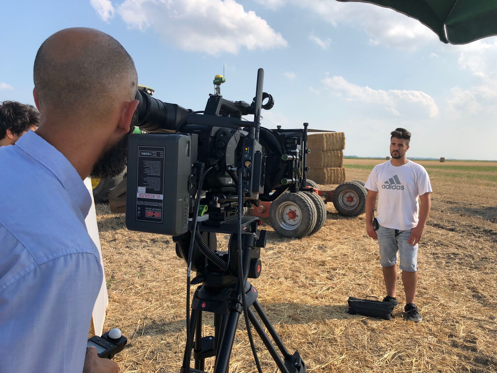 Filming a man standing in a field next to a tractor. The camera operator is focused on the man.