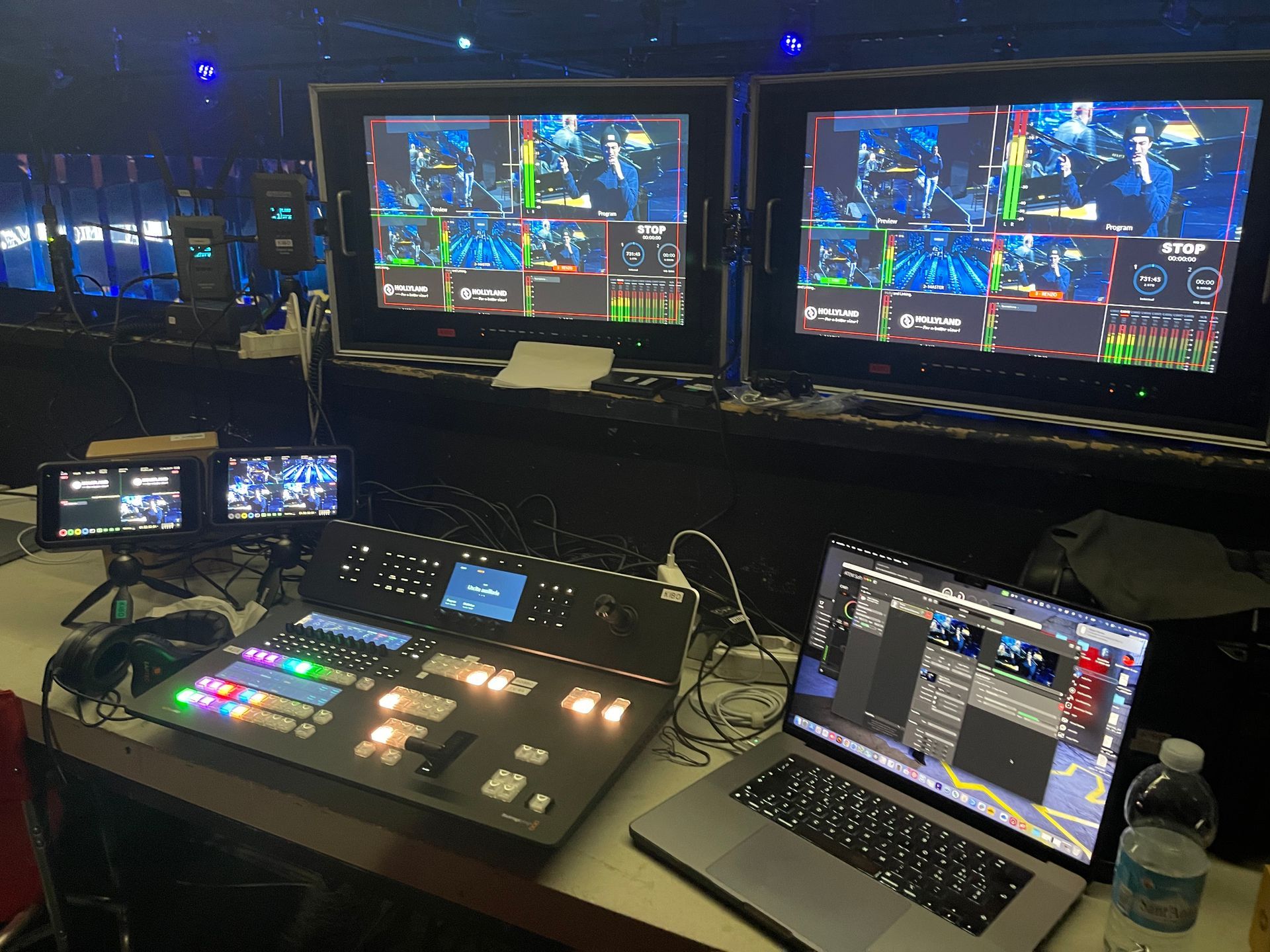 Live event production setup: video monitors, switcher, laptop, and control panel. Black and gray equipment.