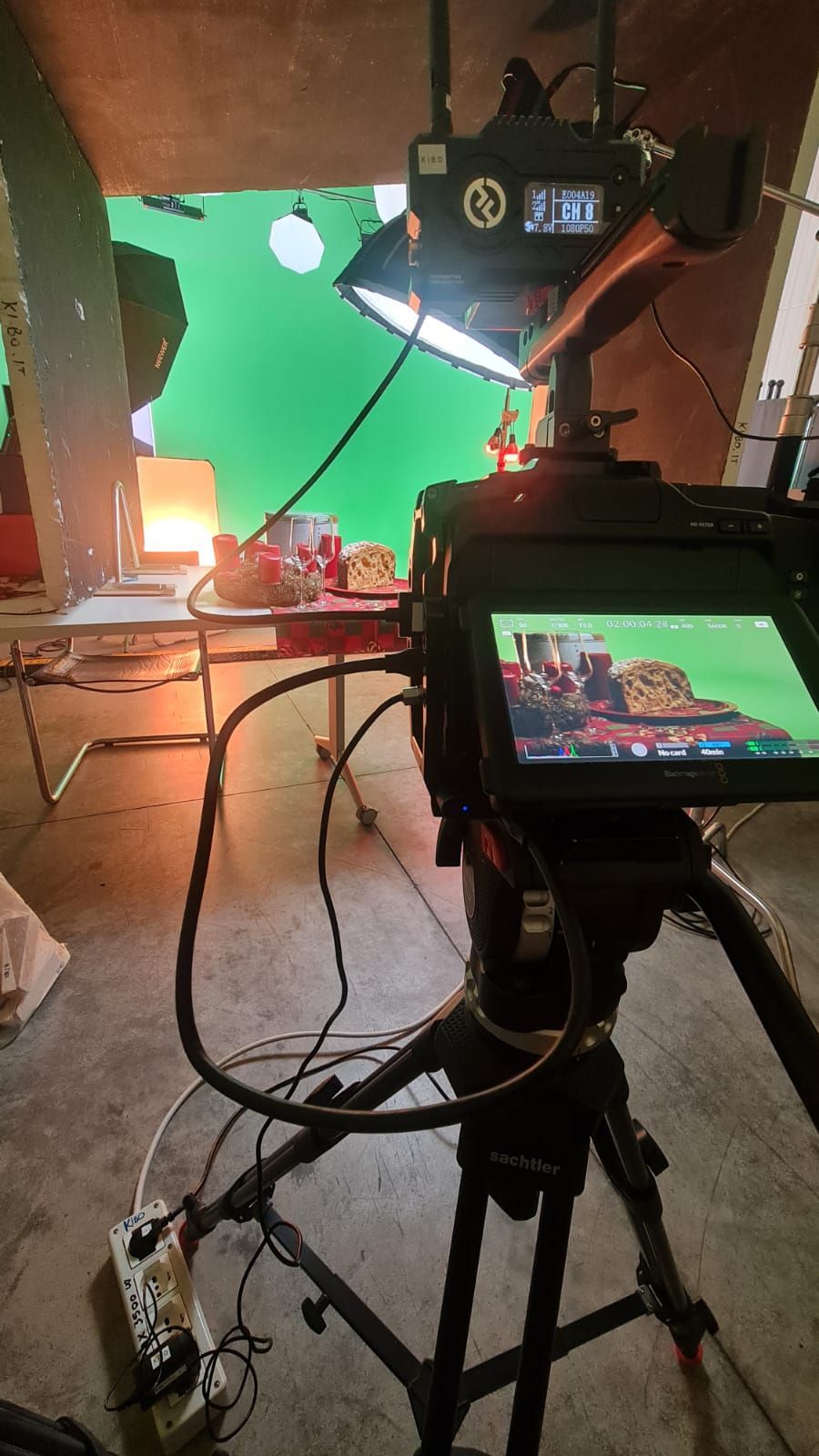 Film set with camera on tripod filming food in front of a green screen, with lights and equipment.