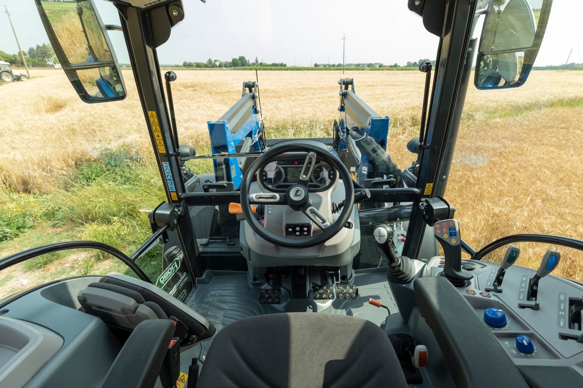 Interior view of a tractor cab with steering wheel, controls, and view of a field.