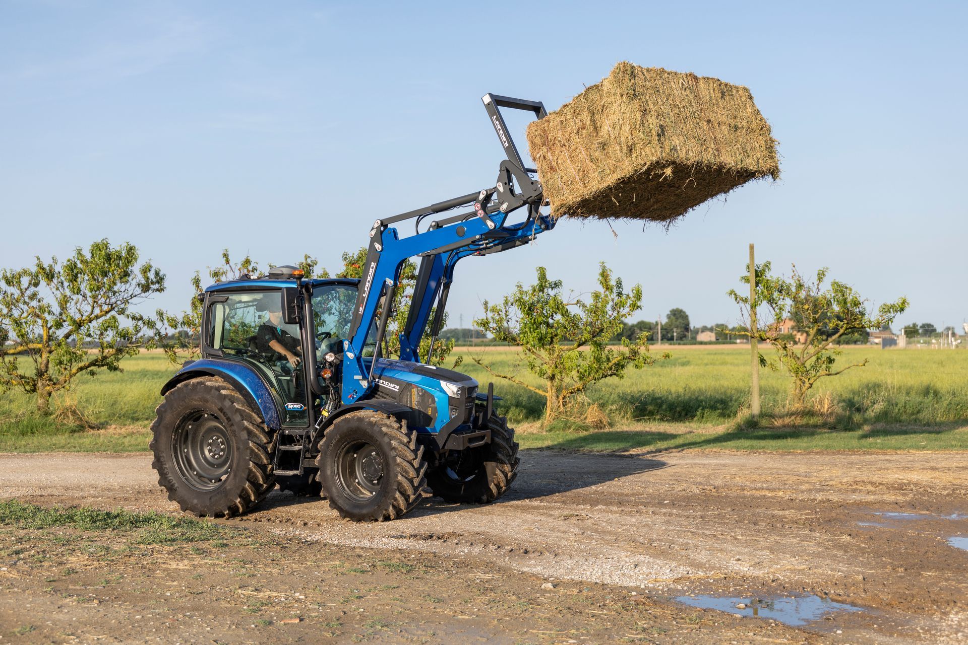 Blue tractor lifting a bale of hay in a field.