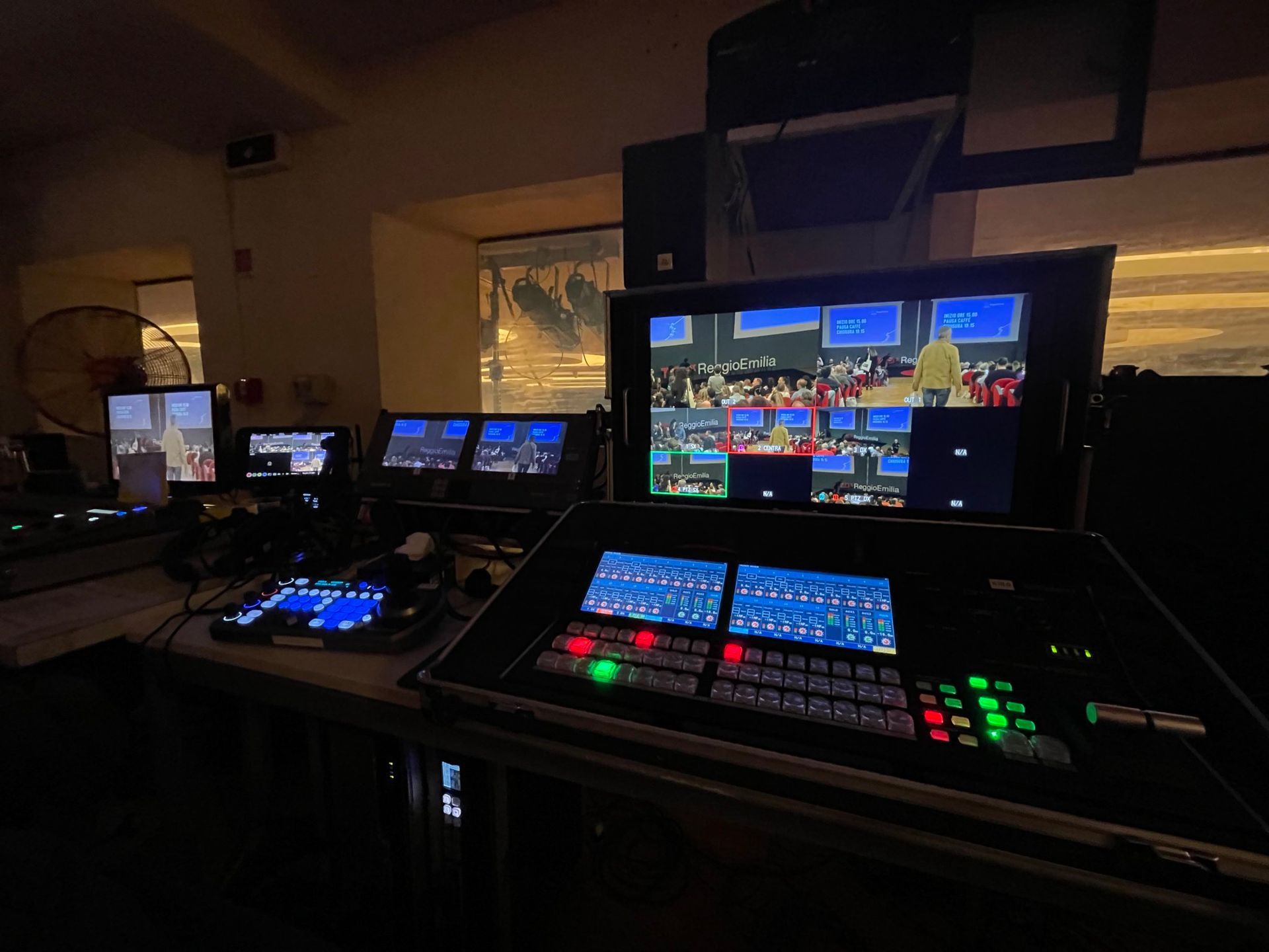 Control room with multiple screens displaying a live event with various camera angles. Lighting equipment is visible.