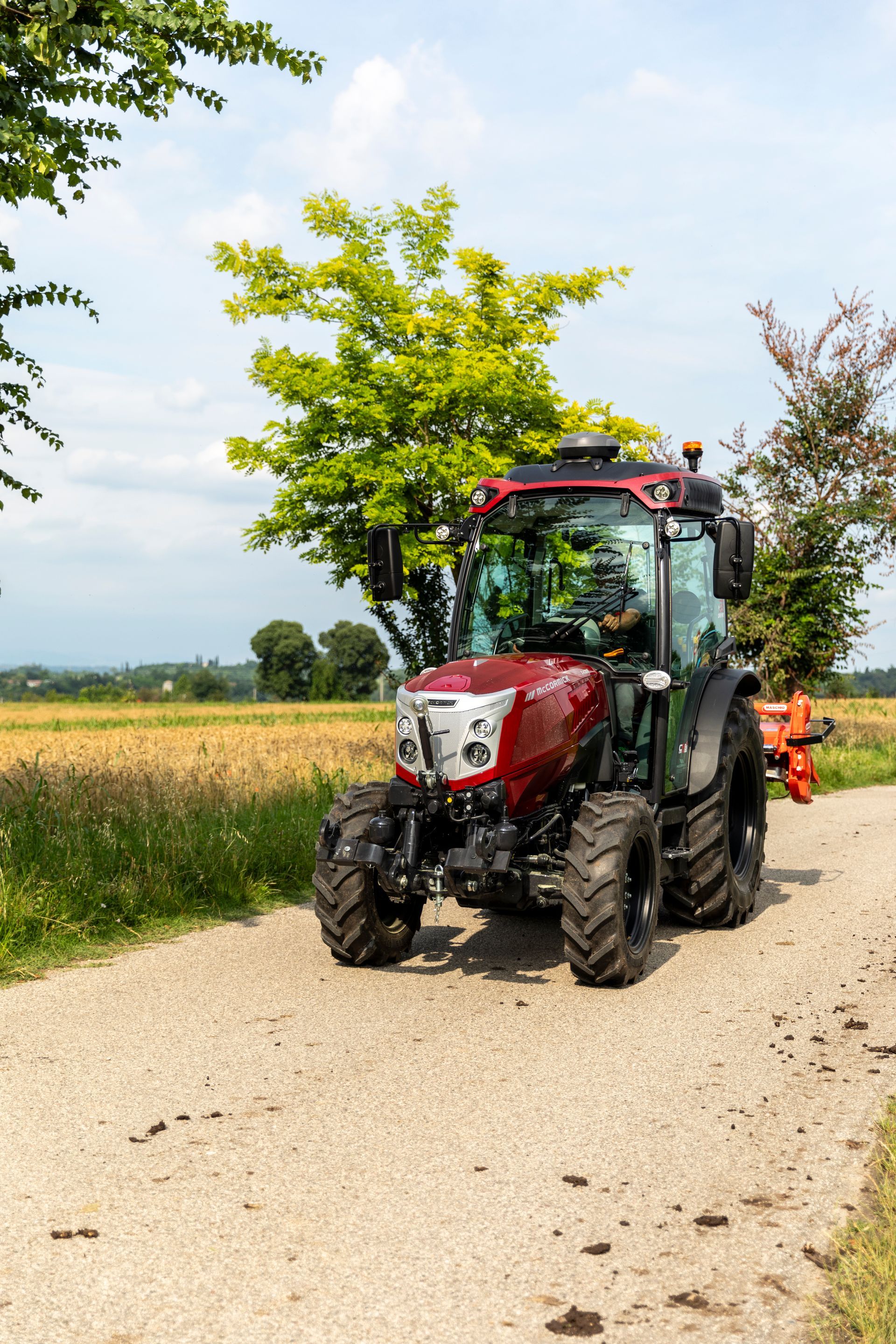 Red tractor on a gravel road, fields in background, sunny day.