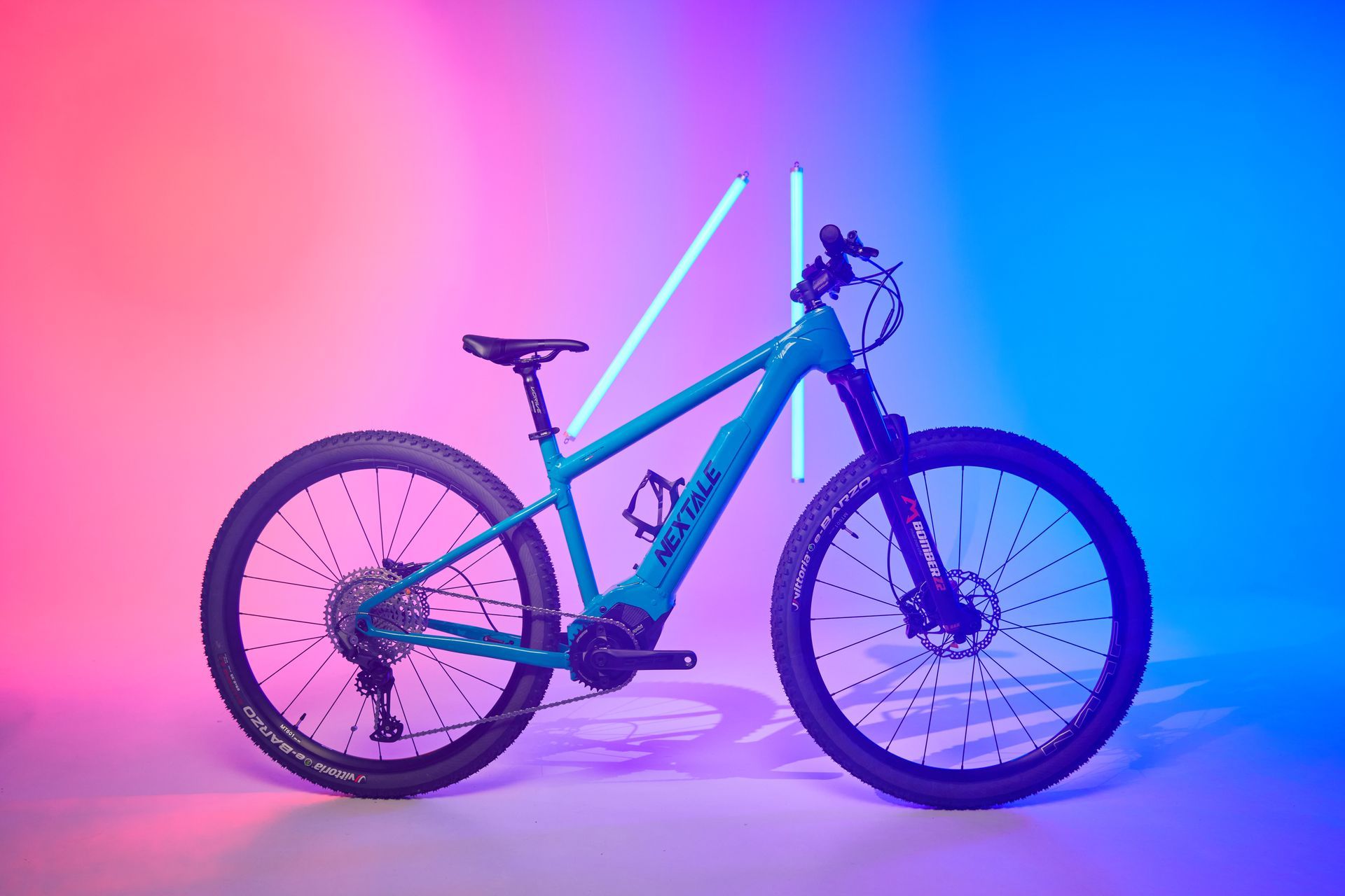 Teal electric mountain bike in a studio setting with pink and blue neon lights.