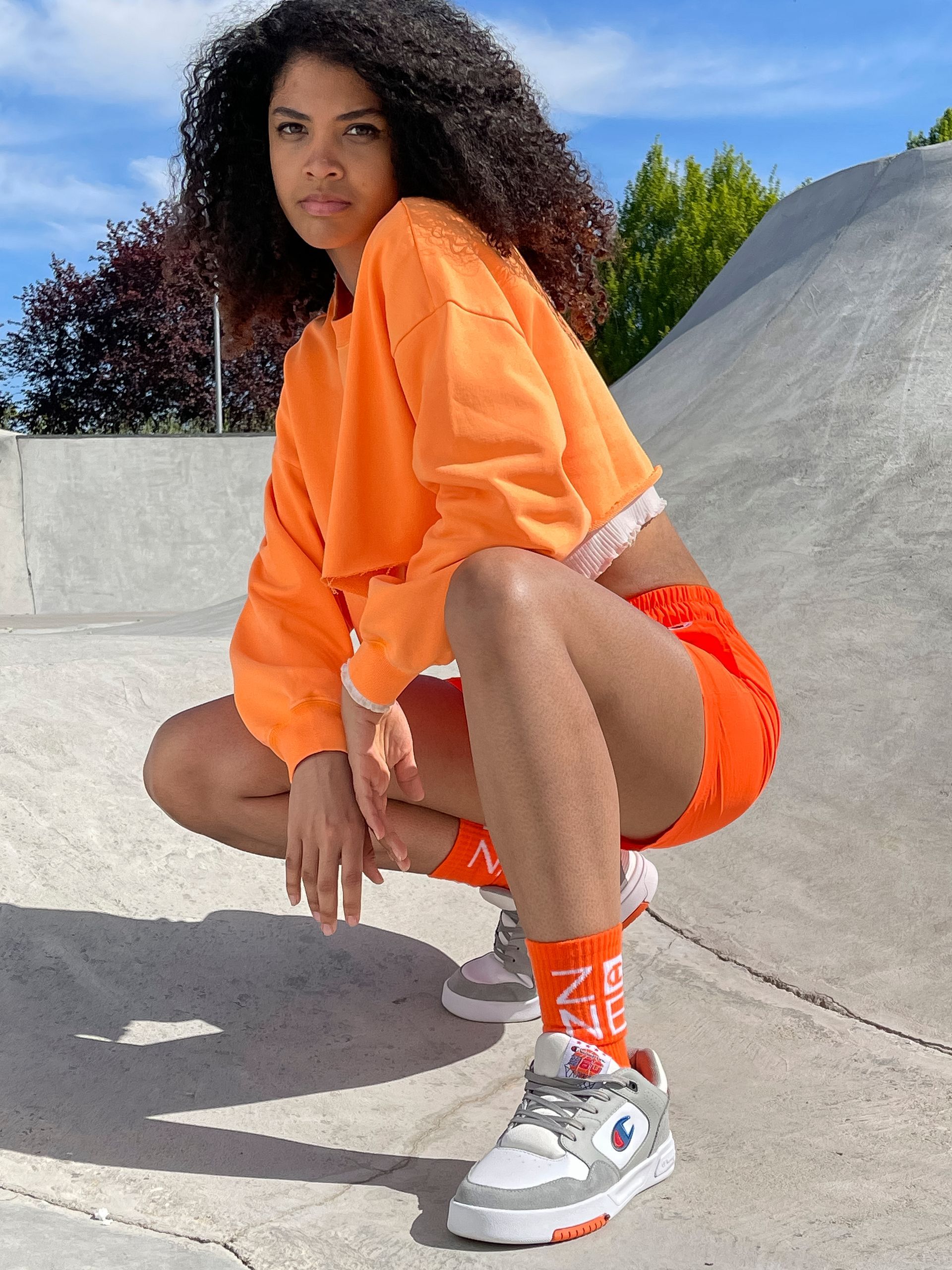 Woman in orange activewear squats at a skate park.