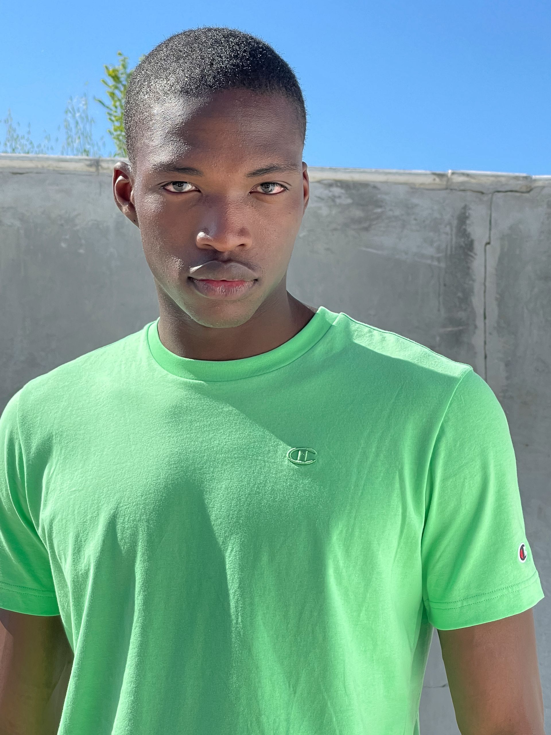 Man in green shirt looking at the camera against a light background.