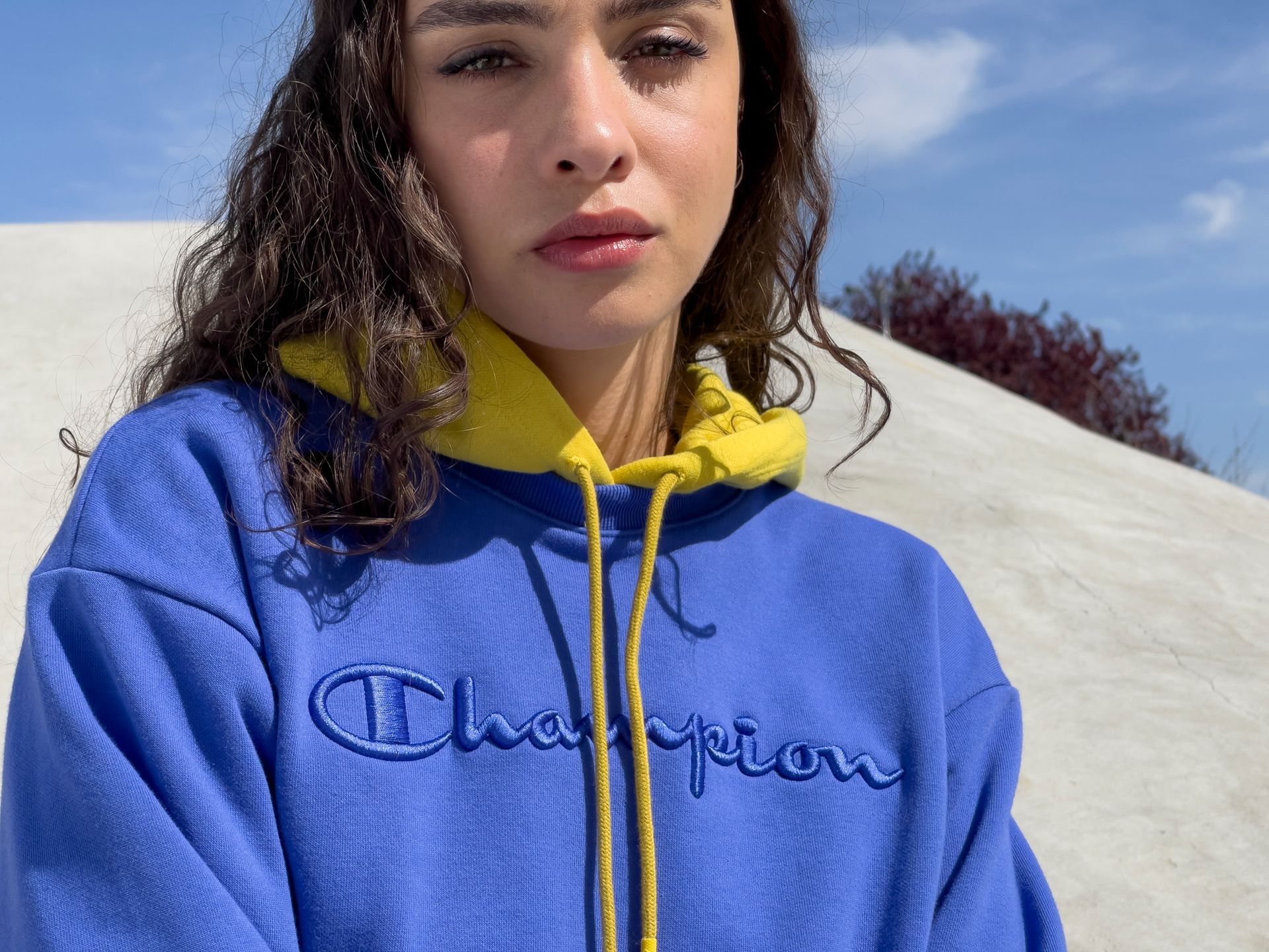 Woman in blue Champion hoodie with yellow lining, looking at the camera outdoors.