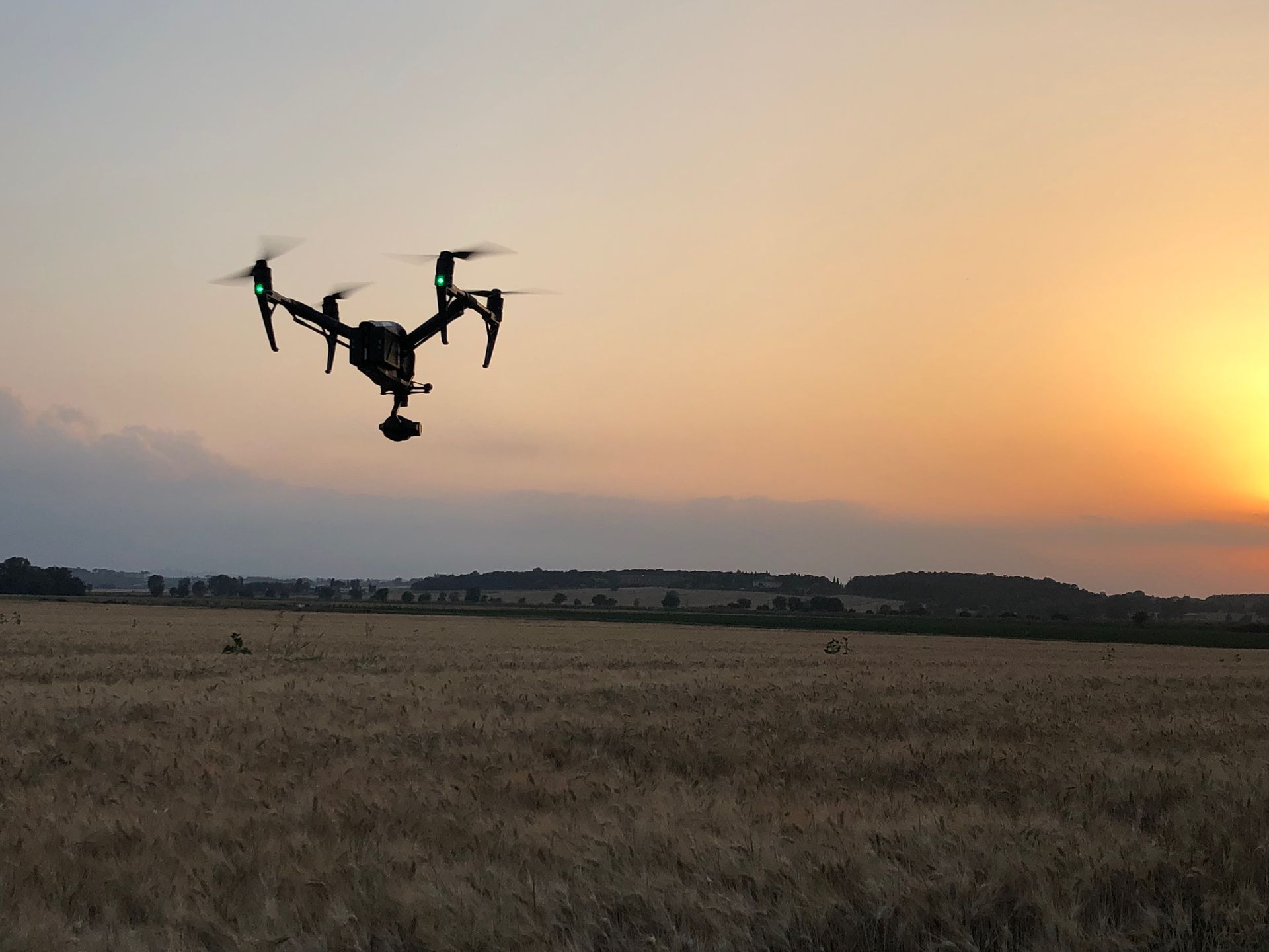Drone flying over a field at sunset, silhouetted against a golden sky.