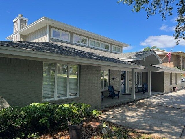 Two-story house with gray siding, windows, and a front porch; blue chairs.