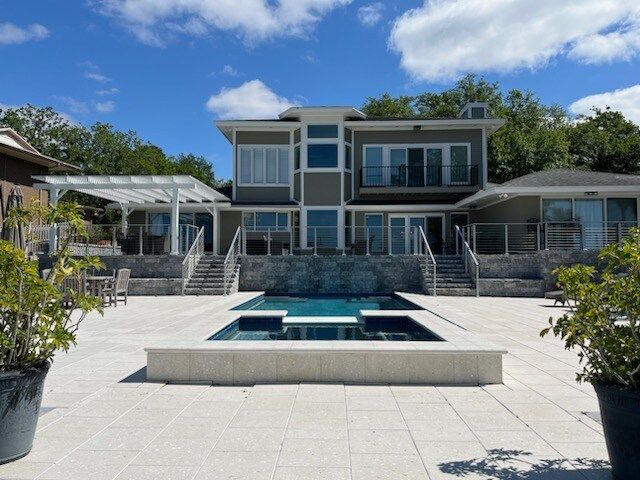 Modern house with a pool, patio, and glass railings. Blue sky, green trees.