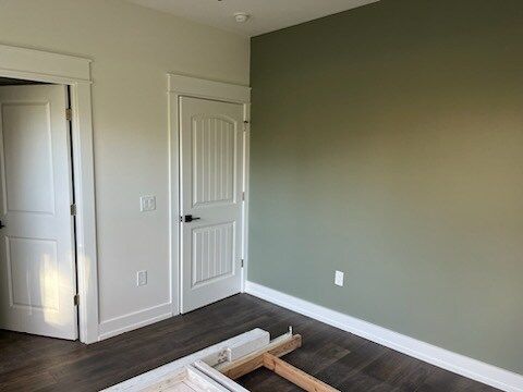 Empty room with dark wood floor, white doors/trim, olive green accent wall.