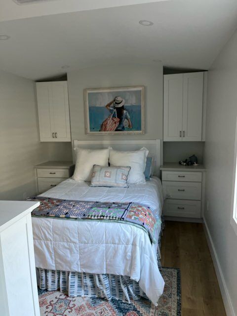 Bedroom with white bed, nightstands, overhead cabinets, and artwork.
