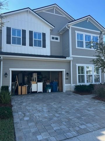 Two-story house with gray siding, blue trim, open garage, and paved driveway.