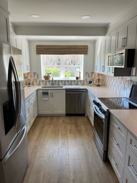 U-shaped kitchen with white cabinets, wood floor, stainless appliances, and patterned backsplash.